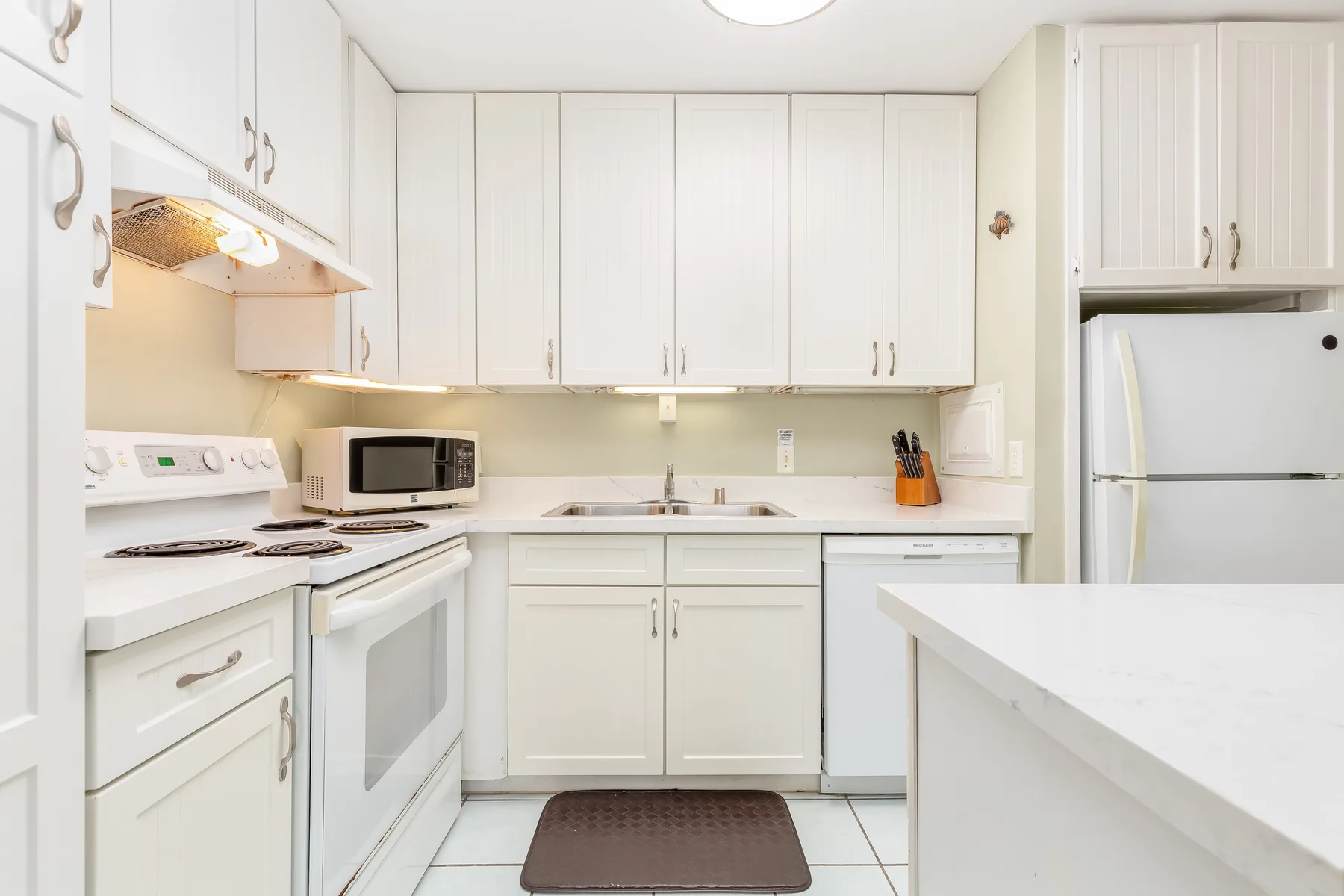 A bright kitchen with white cabinets, appliances, and a central sink.