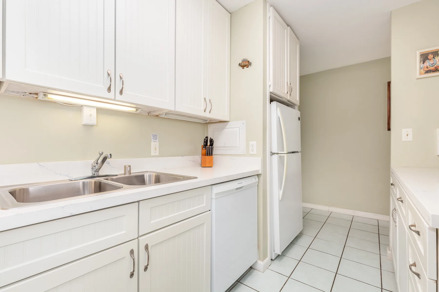 A bright kitchen with white cabinets, a double sink, and a refrigerator.