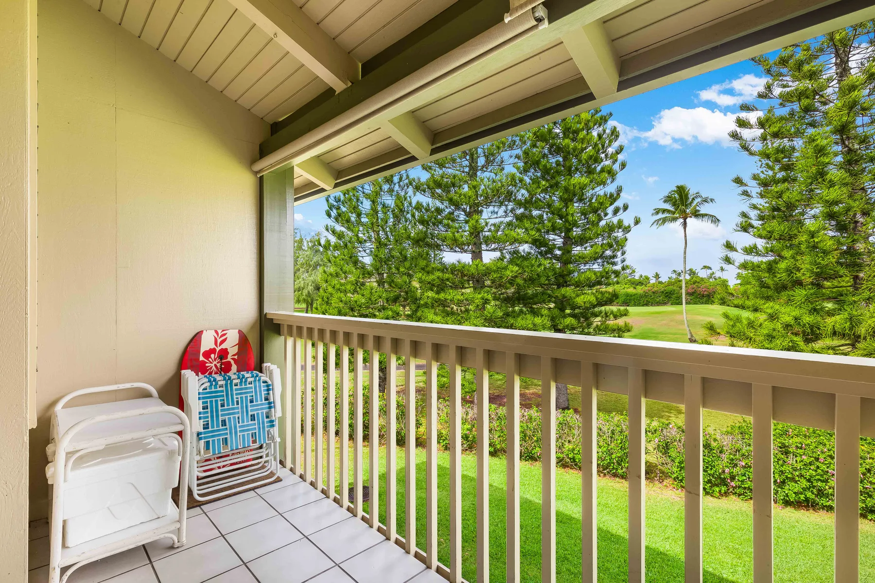A covered balcony with outdoor seating overlooks green lawns and trees.