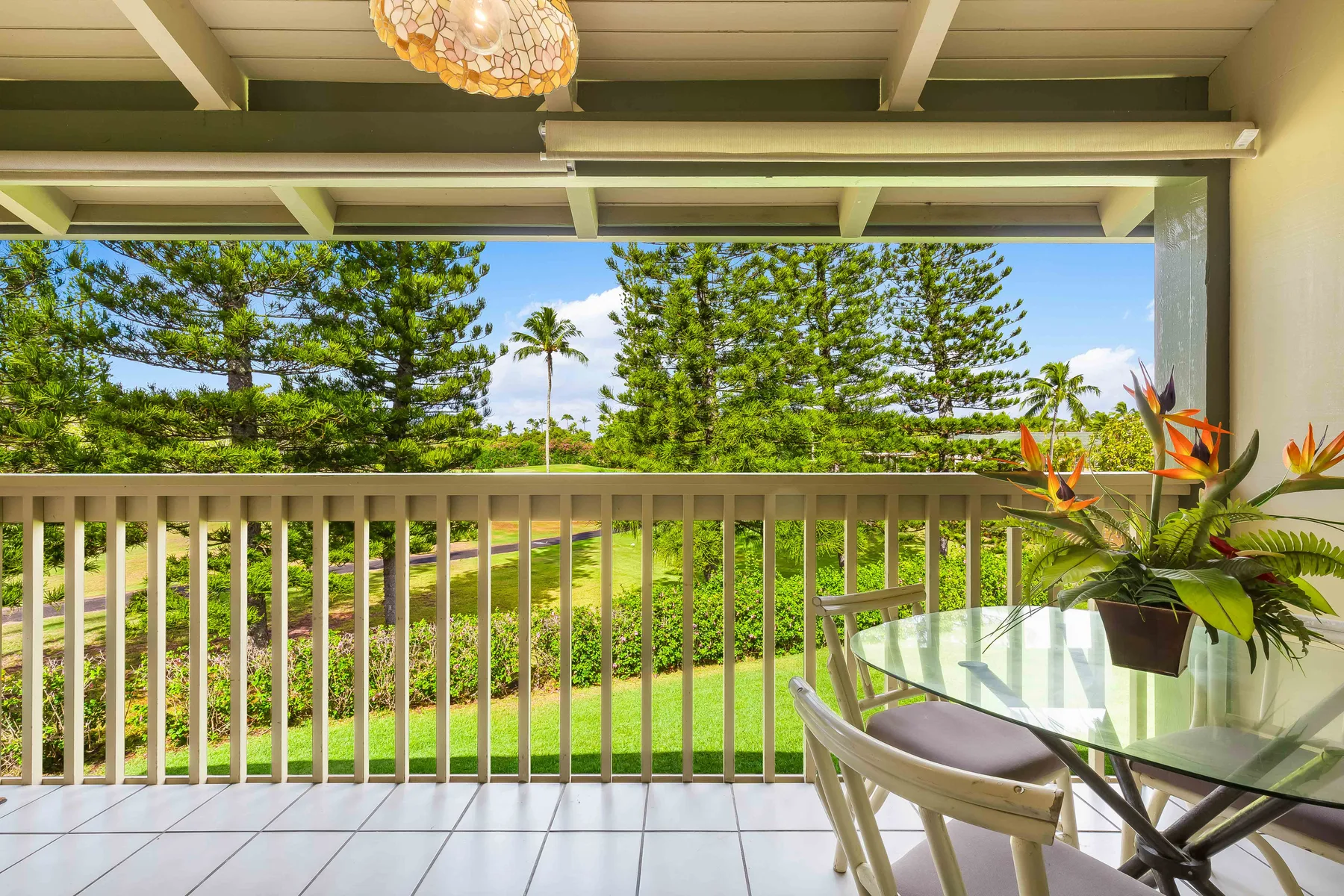A covered balcony with outdoor seating overlooks a green garden.