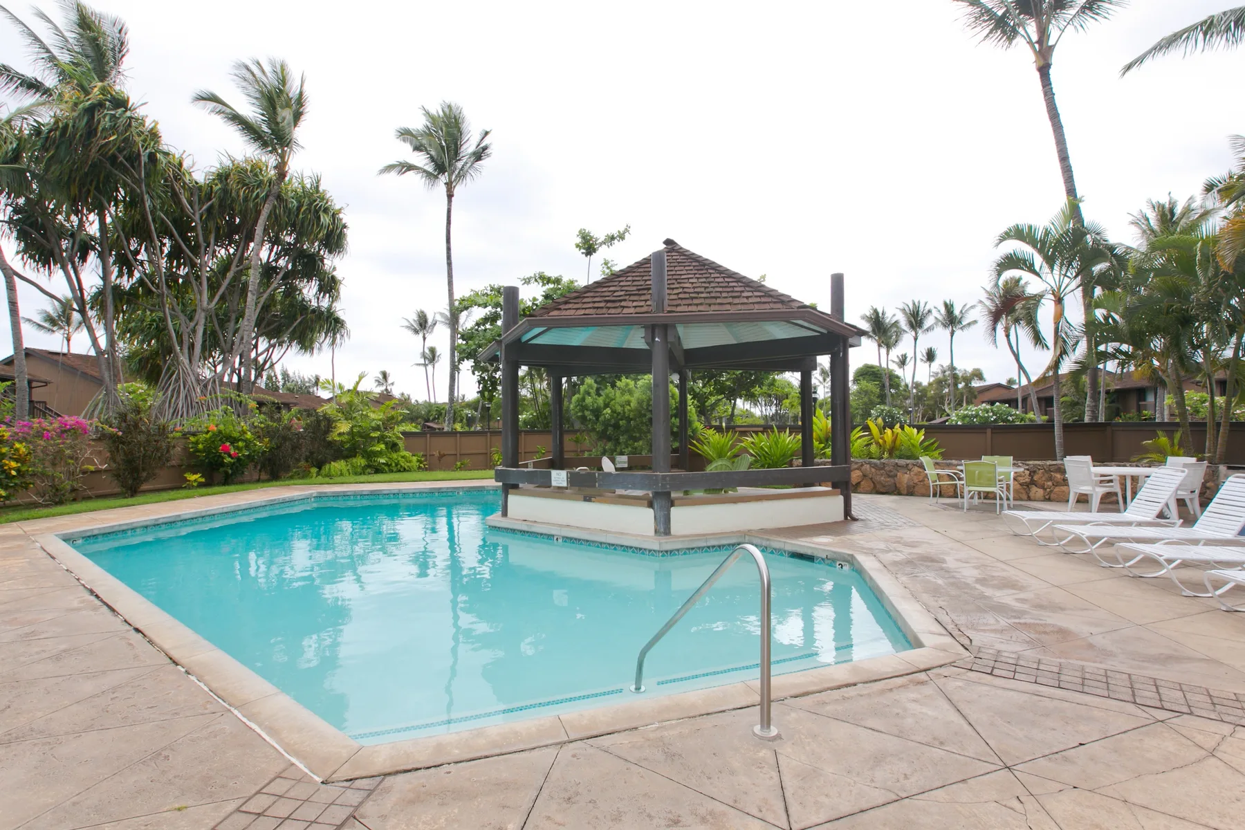 An outdoor swimming pool surrounds a covered pavilion, with lounge seating nearby.