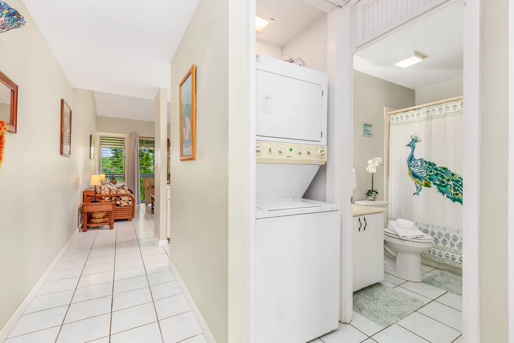 A tiled hallway leads to a laundry area and a bathroom with a peacock-patterned curtain.