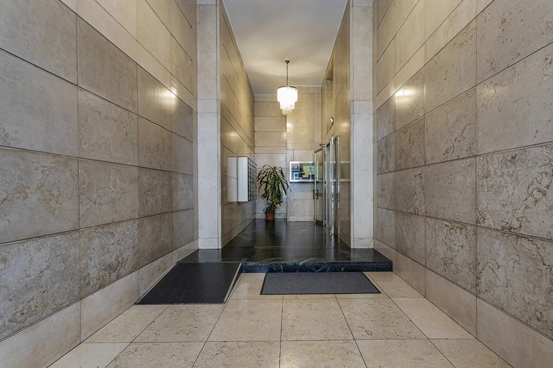 A tiled bathroom entrance opens toward a glass shower and a washbasin.