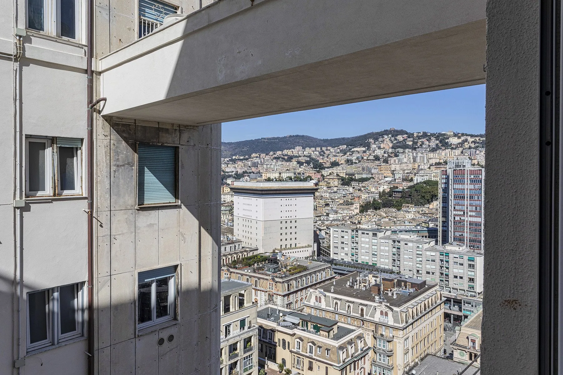 A cityscape of densely packed buildings and hillside homes, viewed through a concrete opening.