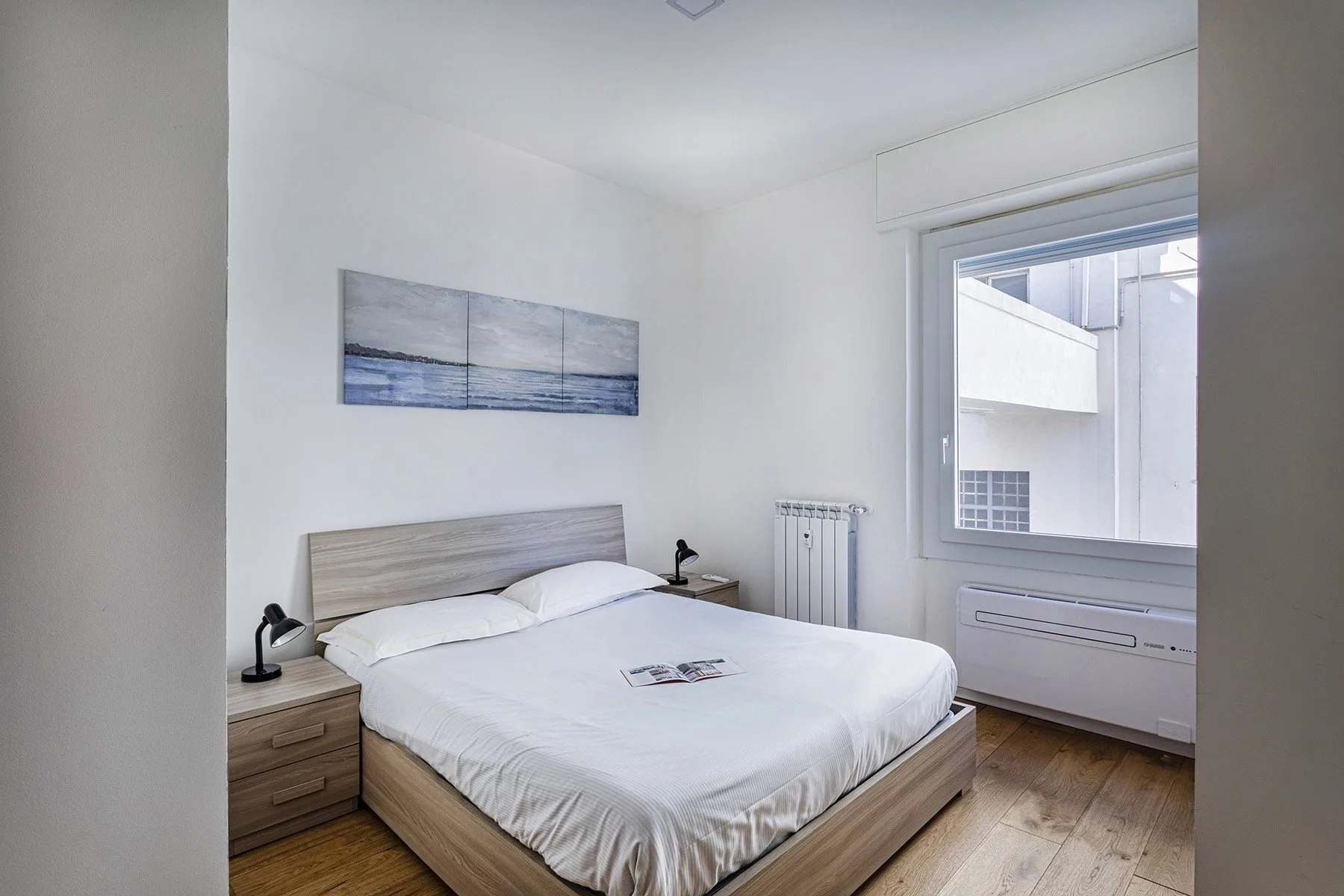 A bright bedroom with a neatly made bed and a large window.