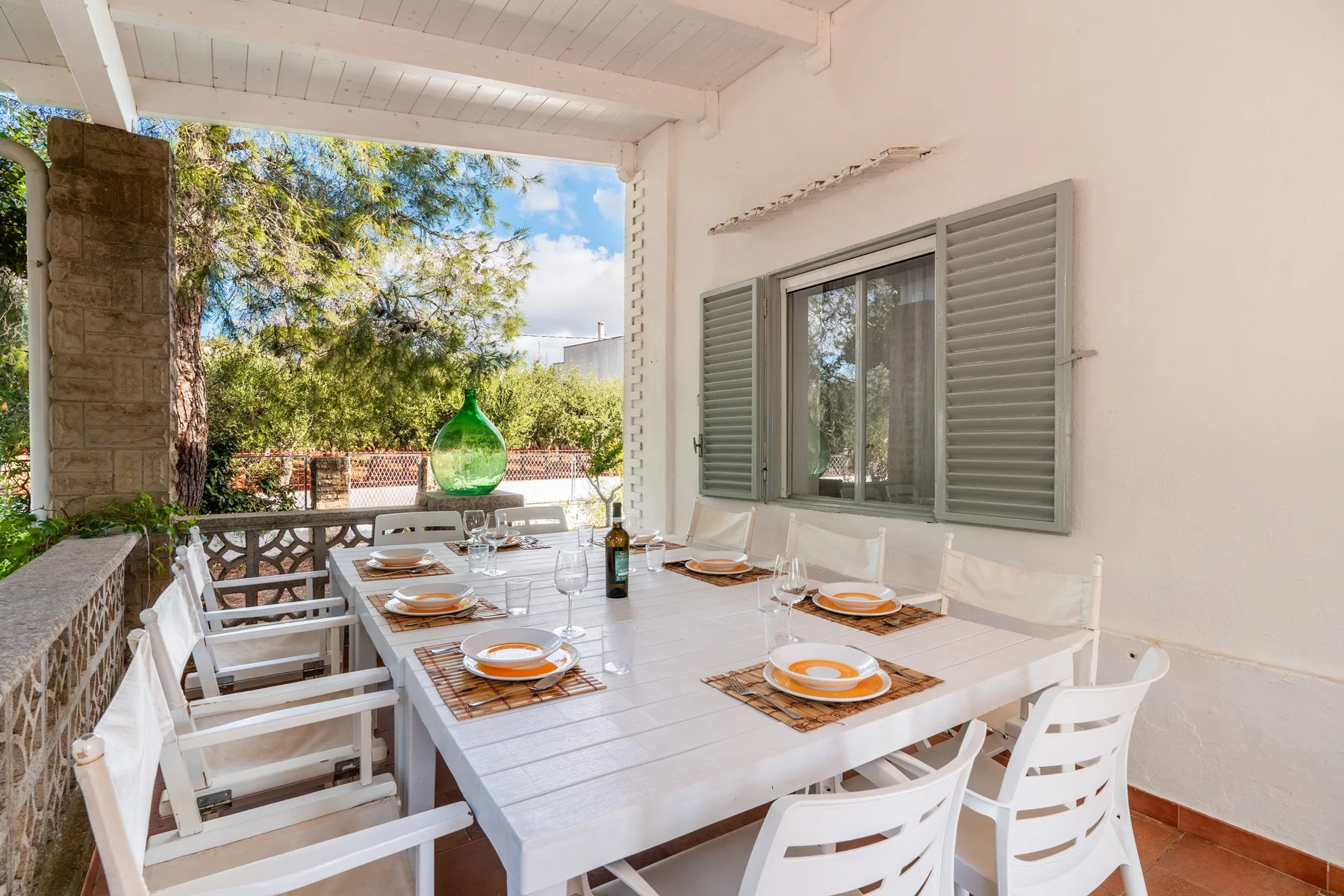A covered outdoor dining area with a long table and white seating.