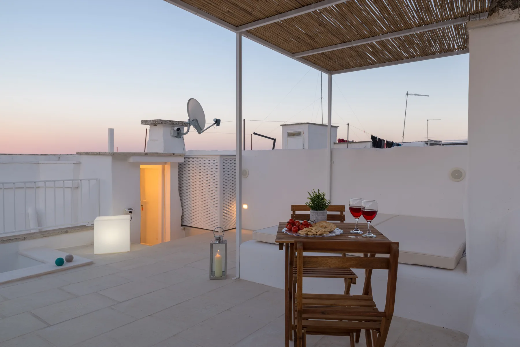 Una terraza en la azotea con una mesa de comedor de madera y asientos bajo un toldo de listones.