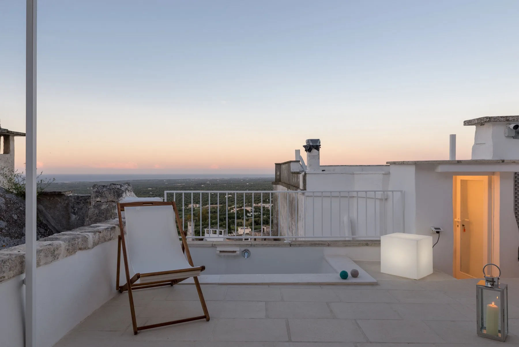 Una terraza en la azotea al atardecer tiene una silla de descanso junto a una pequeña piscina.