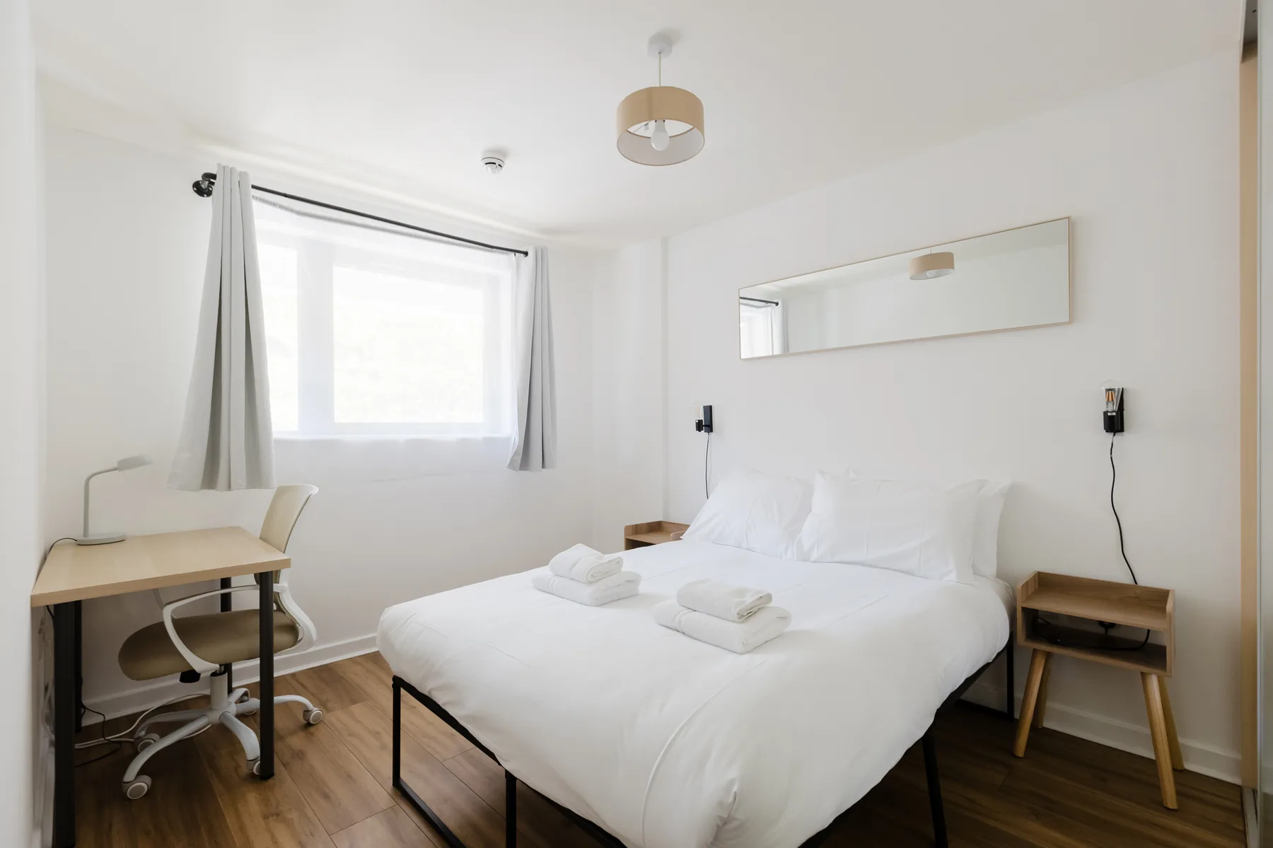Un dormitorio luminoso con una cama bien arreglada y un escritorio junto a la ventana.