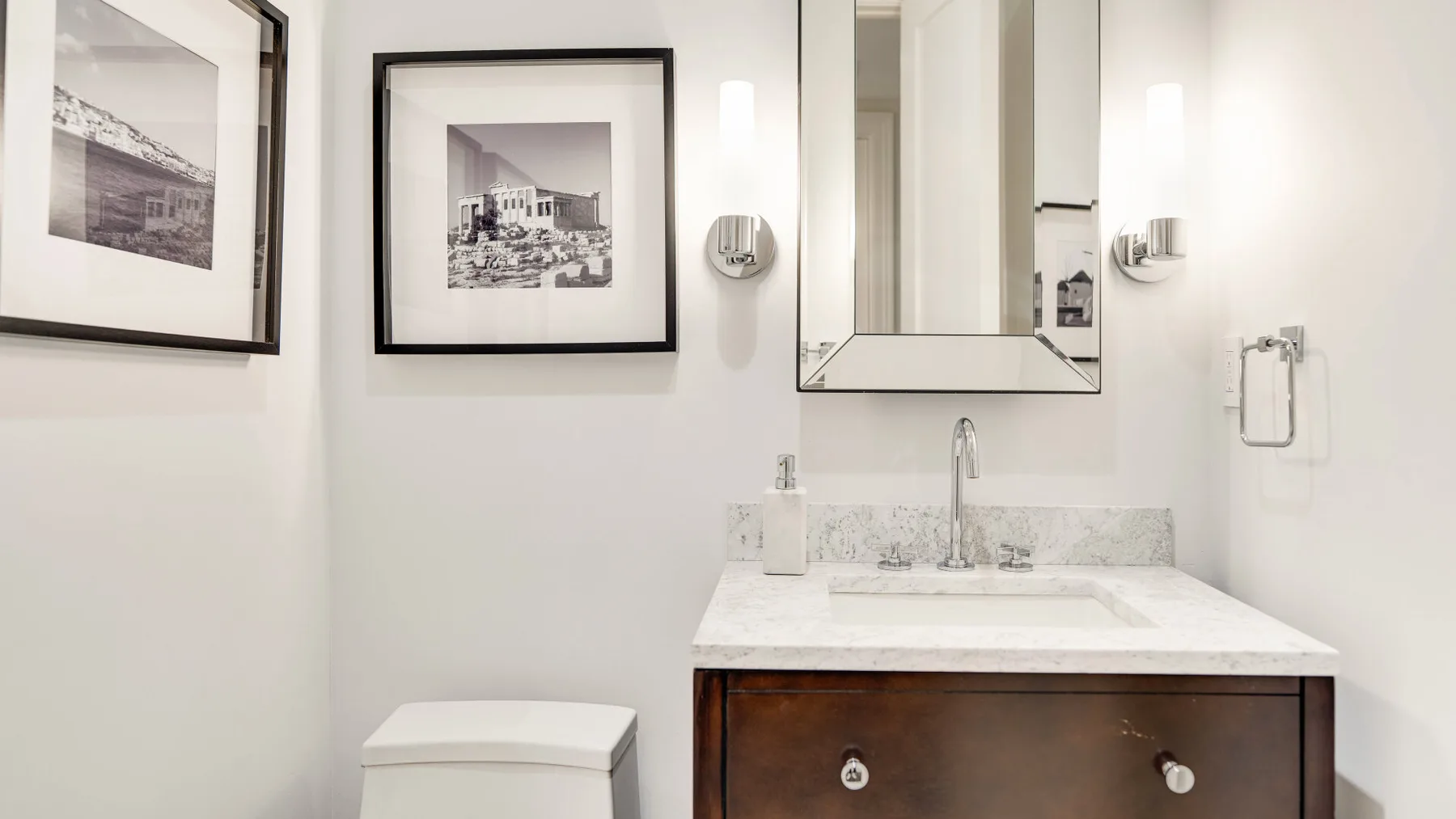 Un tocador de baño luminoso con espejo de pared y fotografías enmarcadas.