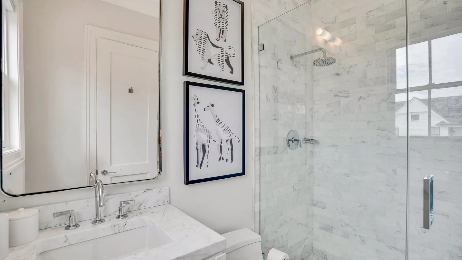 Un baño luminoso con lavabo, cuadros enmarcados y una ducha de vidrio.