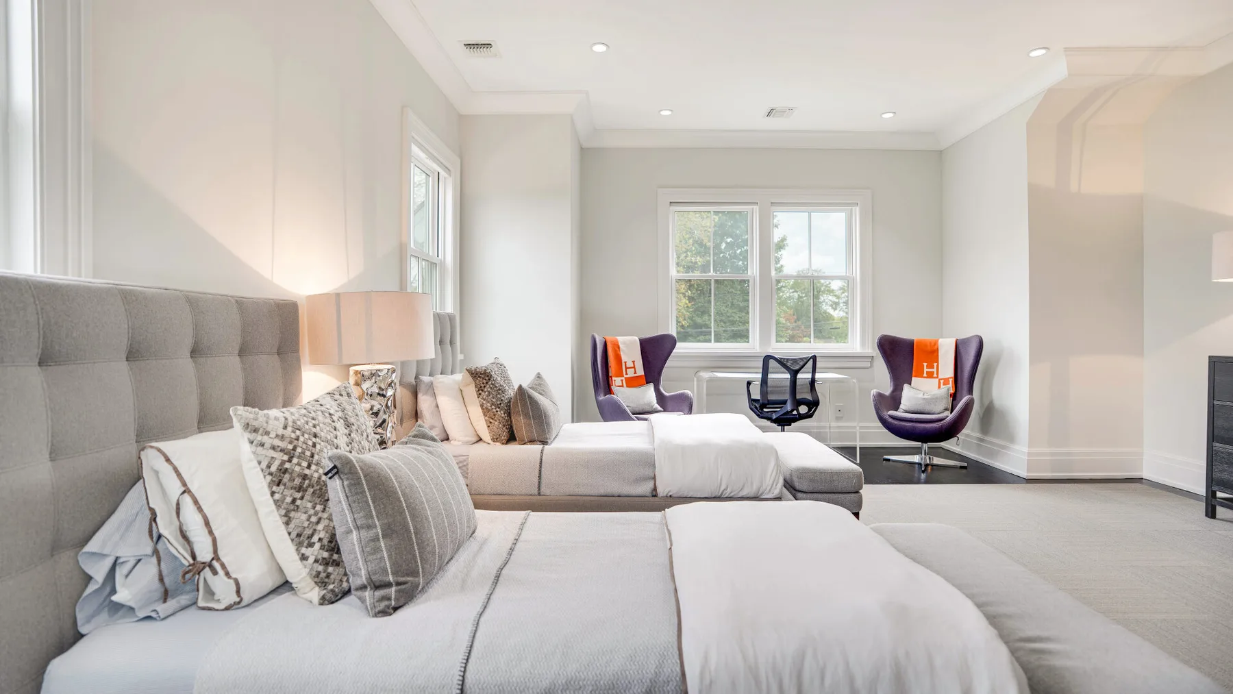 Un dormitorio luminoso con una cama grande y dos sillones junto a la ventana.