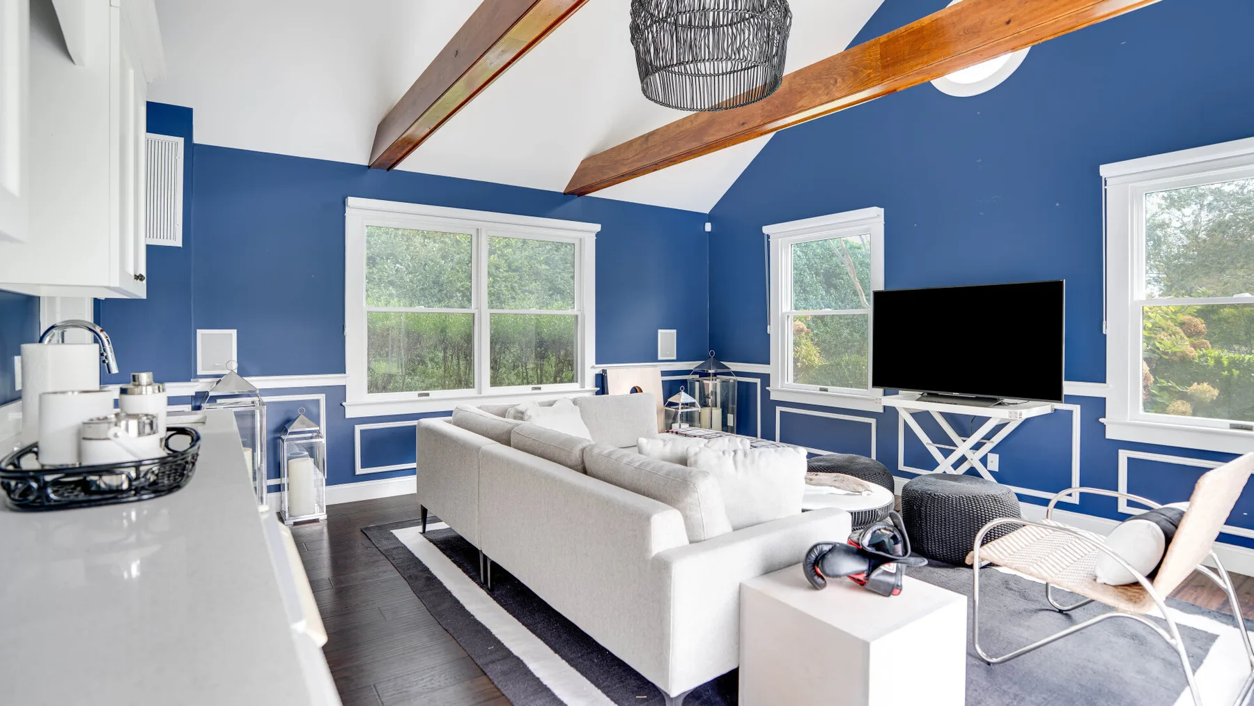 Una sala de estar luminosa con paredes azules, asientos blancos y ventanas grandes.