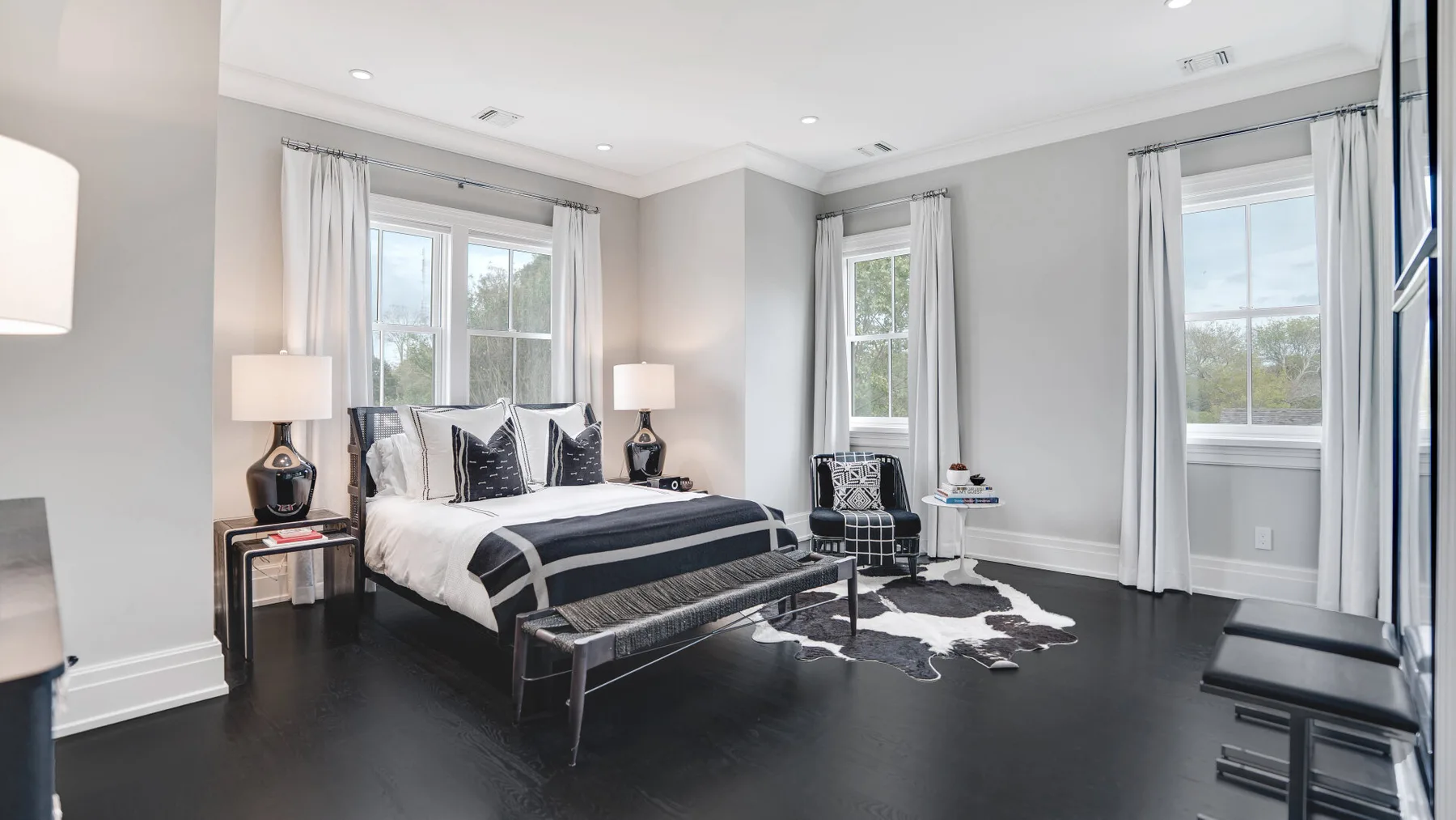 Un dormitorio luminoso con una cama grande, ventanas altas y cortinas claras.
