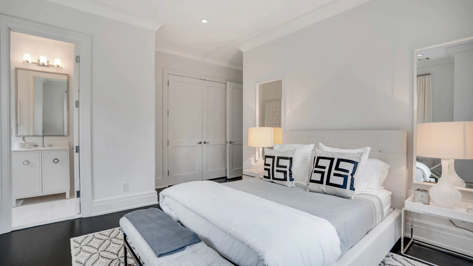 Un dormitorio luminoso con una cama bien tendida y un tocador con espejo.