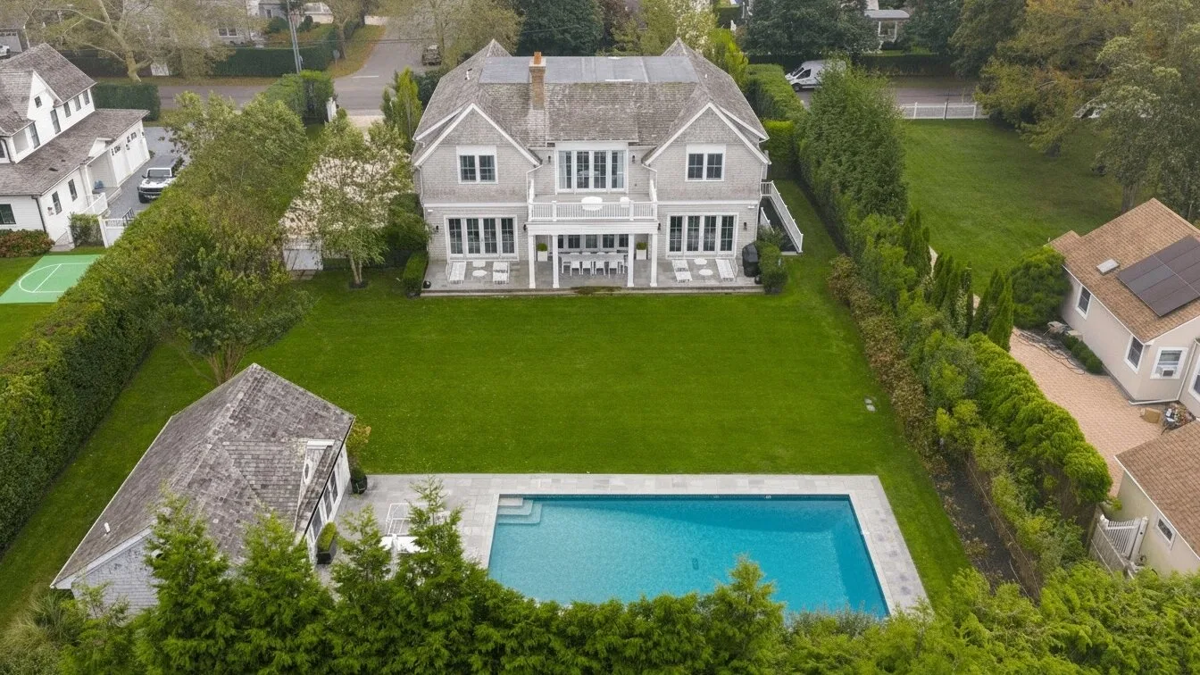 Una vista aérea muestra una casa grande, un amplio césped verde y una piscina.
