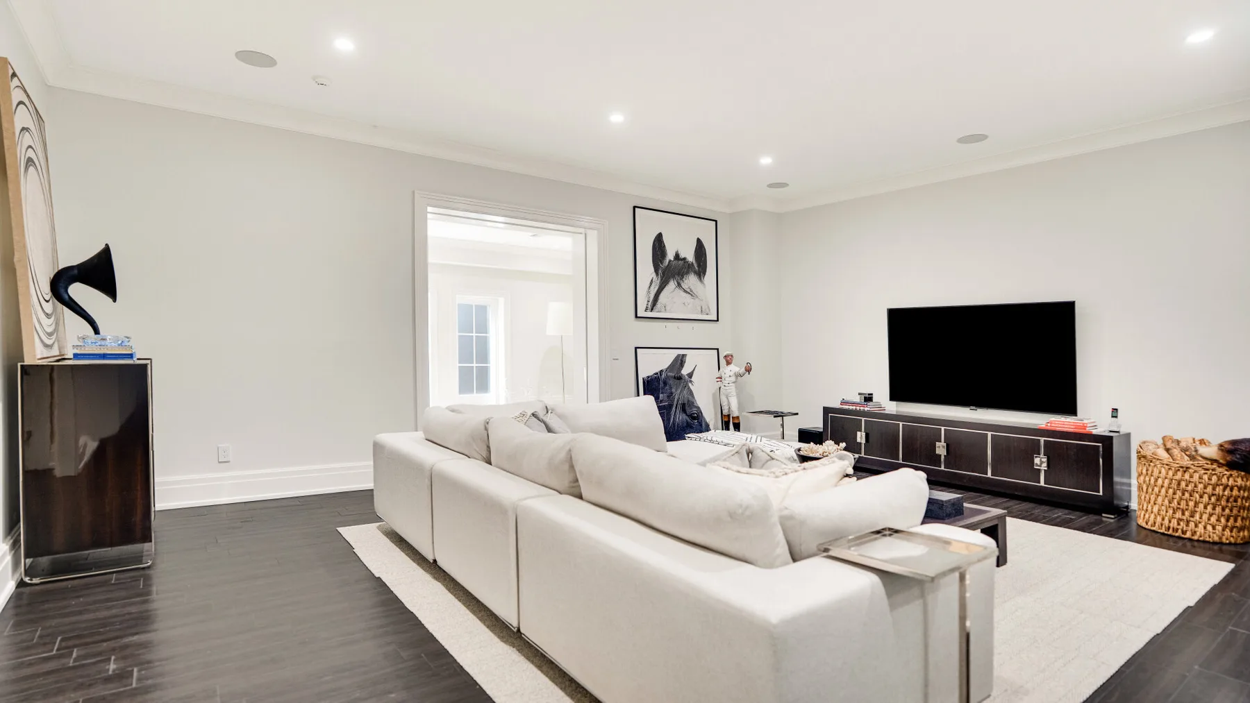 Una sala luminosa con asientos blancos, un televisor y una alfombra clara.