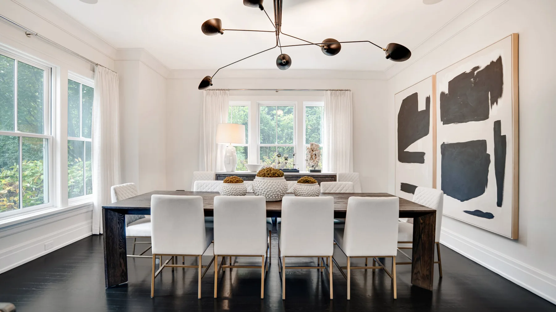 Un comedor luminoso con una mesa larga, asientos blancos y una gran obra abstracta.