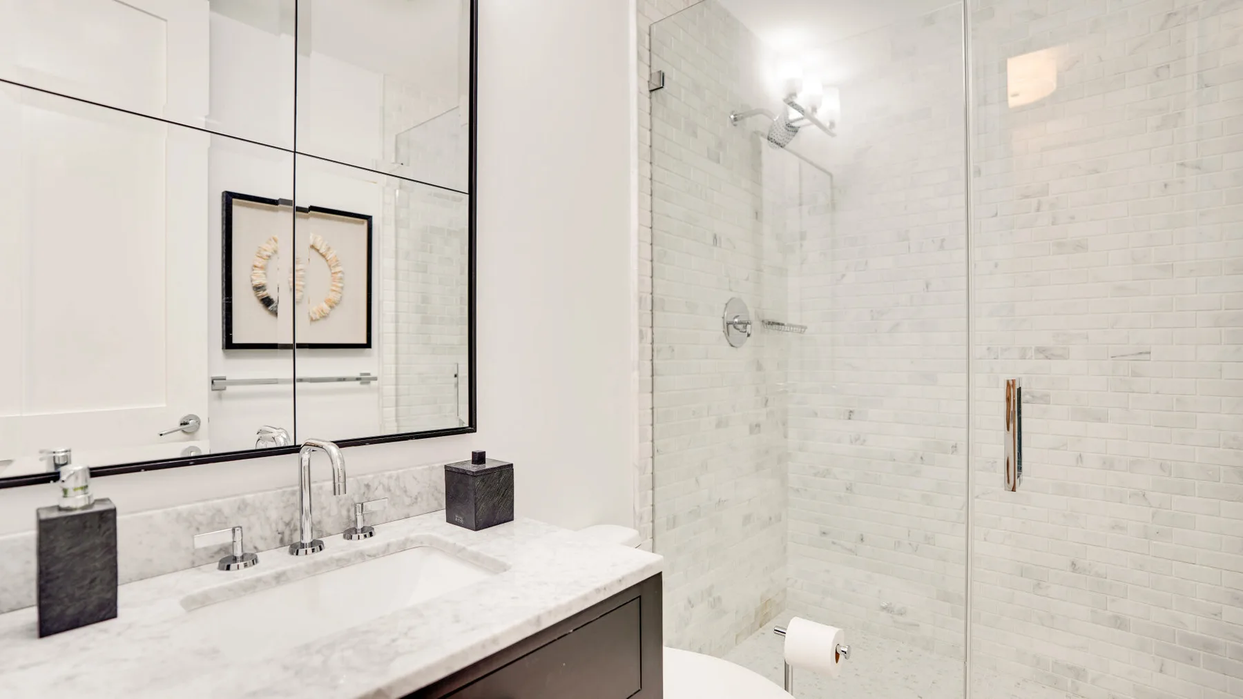 Un baño luminoso con lavabo de mármol y ducha con mampara de vidrio.