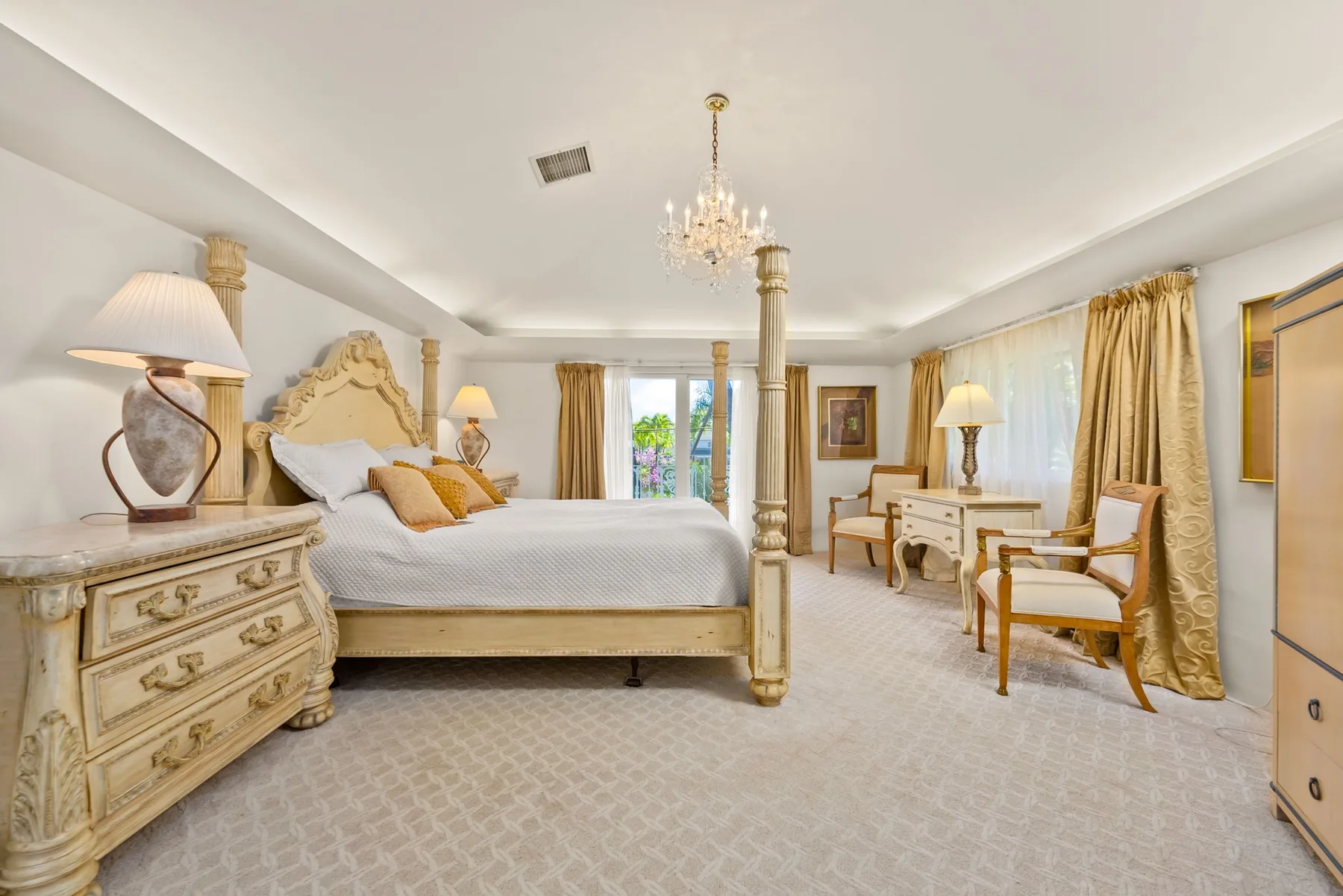 Un dormitorio con una cama grande, muebles junto a ella y una zona de estar junto a las ventanas.