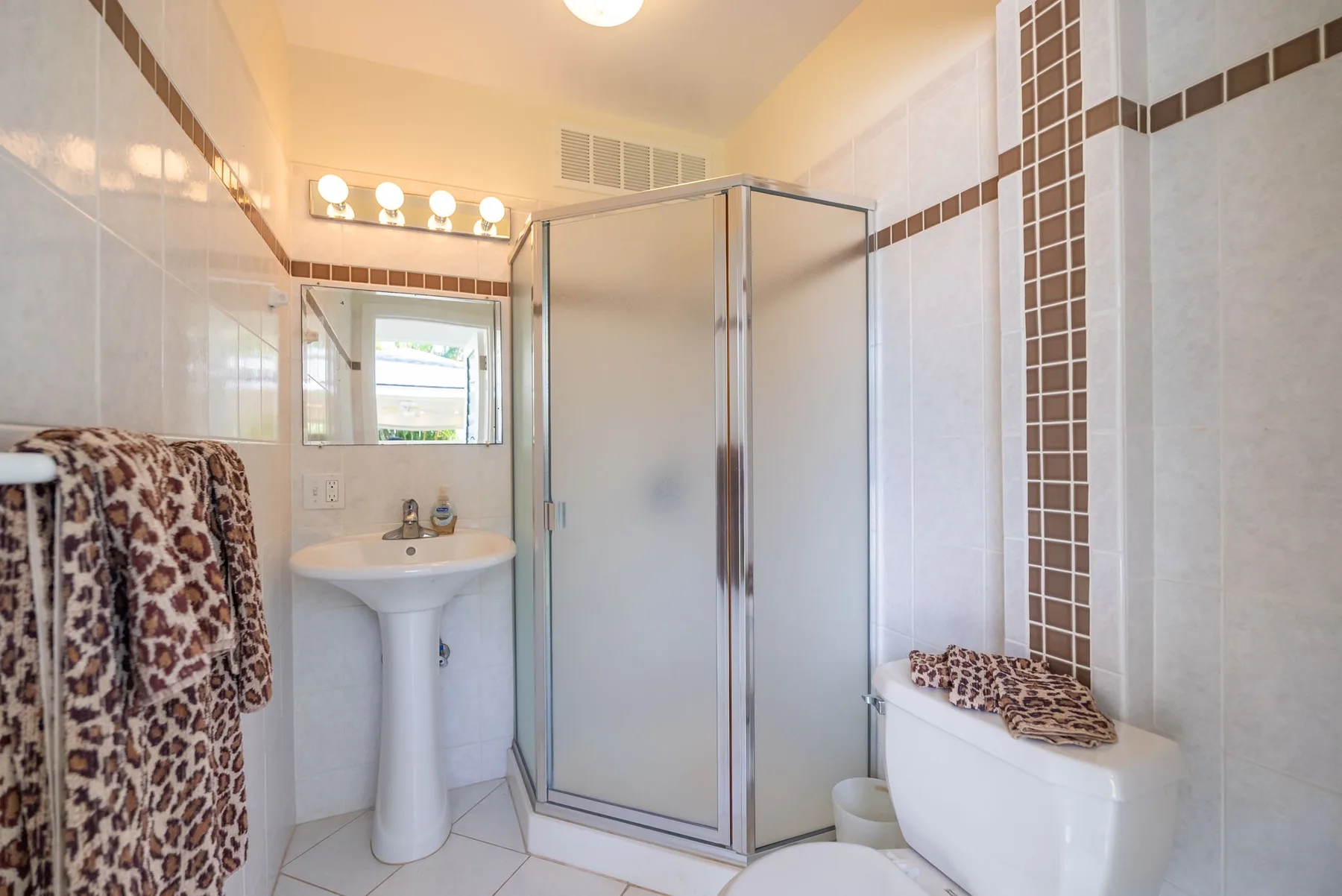 Un baño con azulejos, ducha de vidrio, lavabo de pedestal e inodoro.