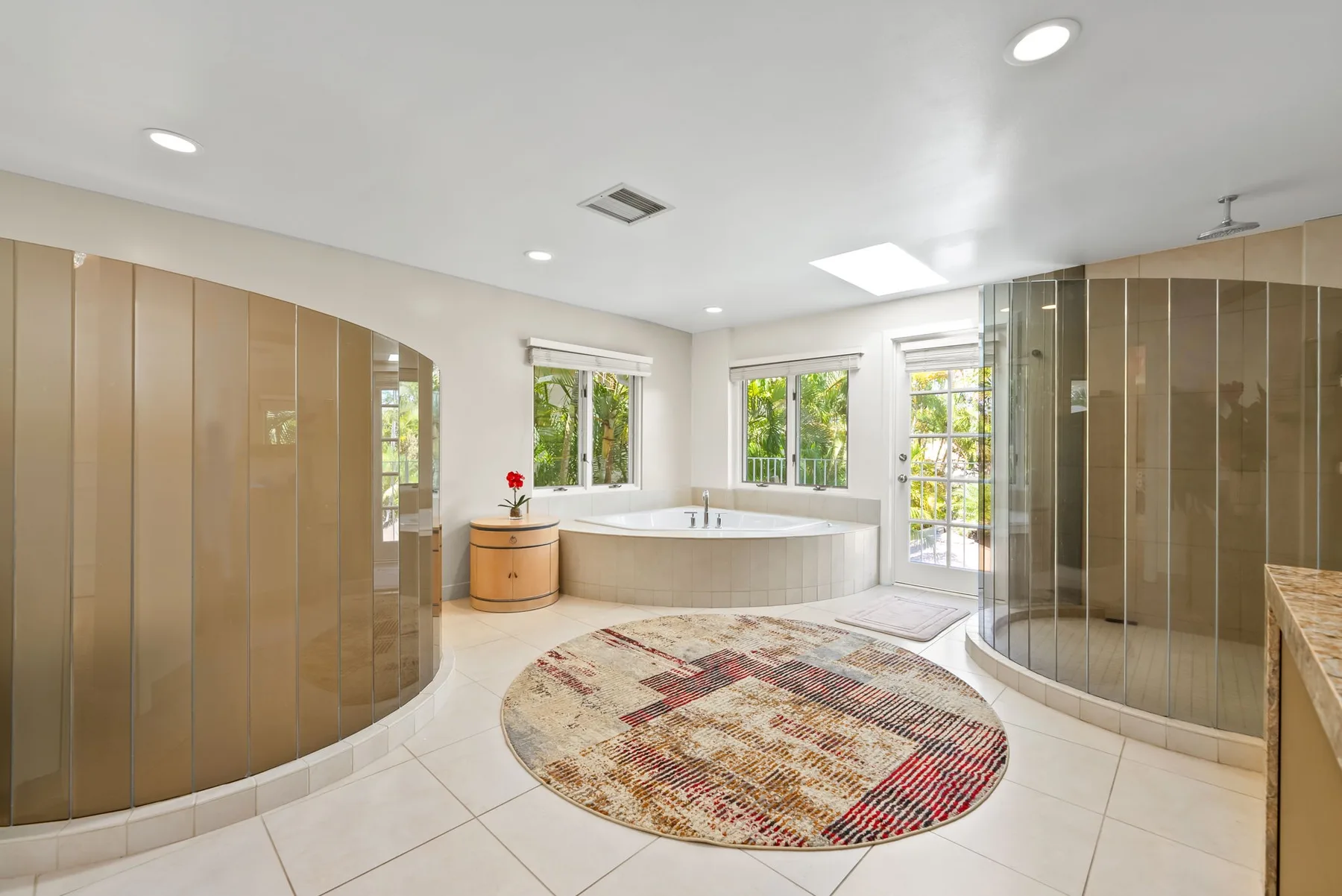 Un baño luminoso con bañera, duchas de vidrio y ventanas con vistas a la vegetación.