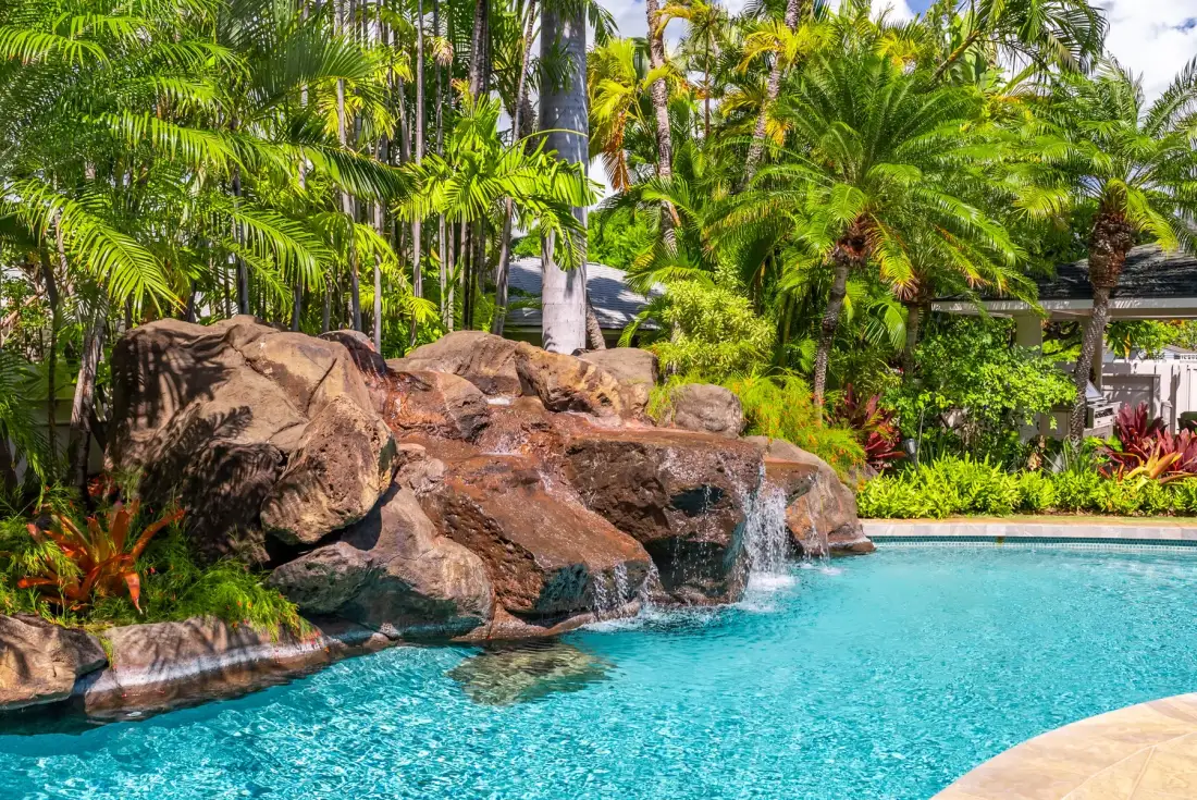 Una piscina rodeada de rocas, cascadas y plantas tropicales.