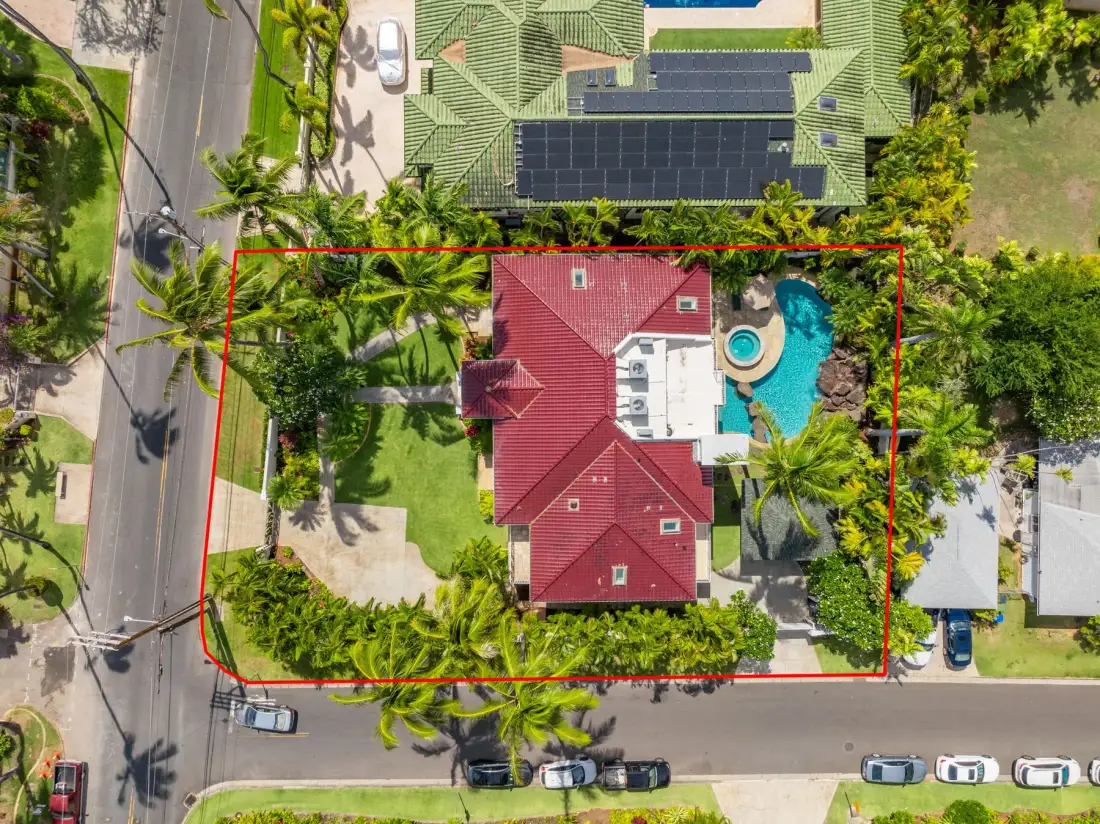 Vista aérea de una casa con techo rojo junto a una piscina y palmeras.