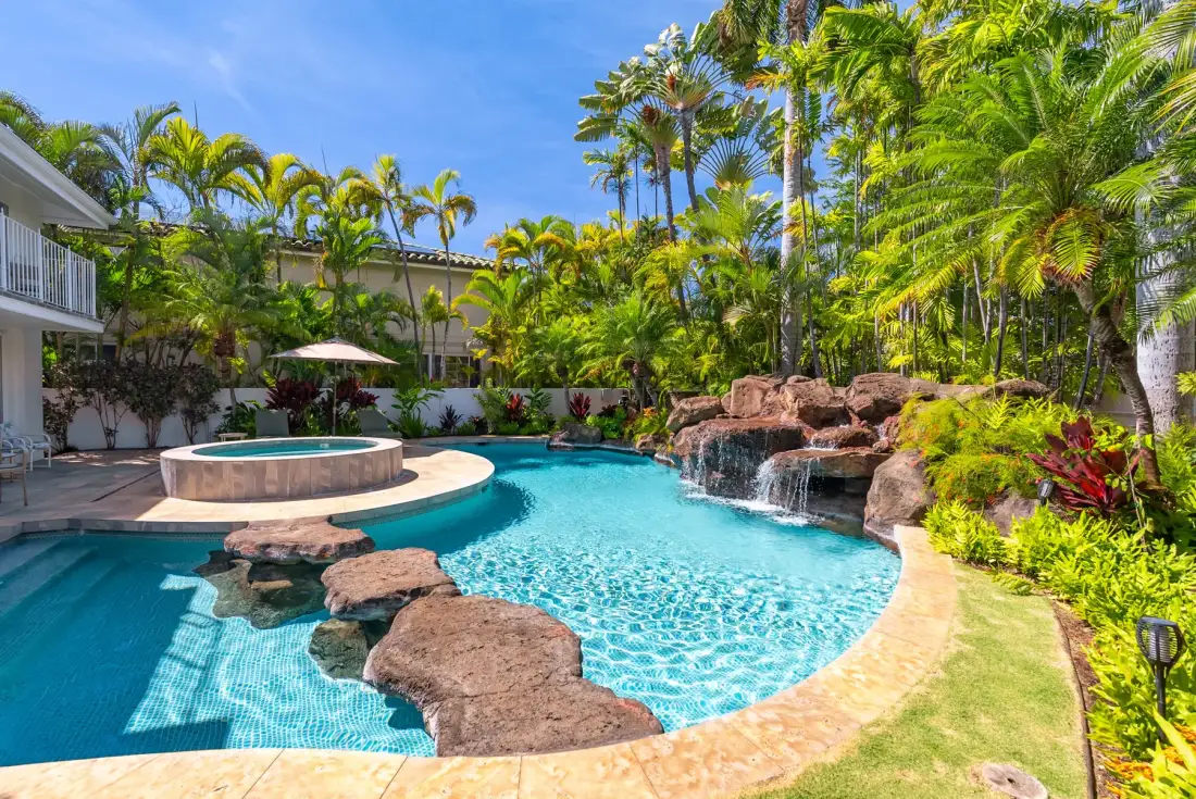 A tropical outdoor pool with a raised circular spa and a small rock waterfall.