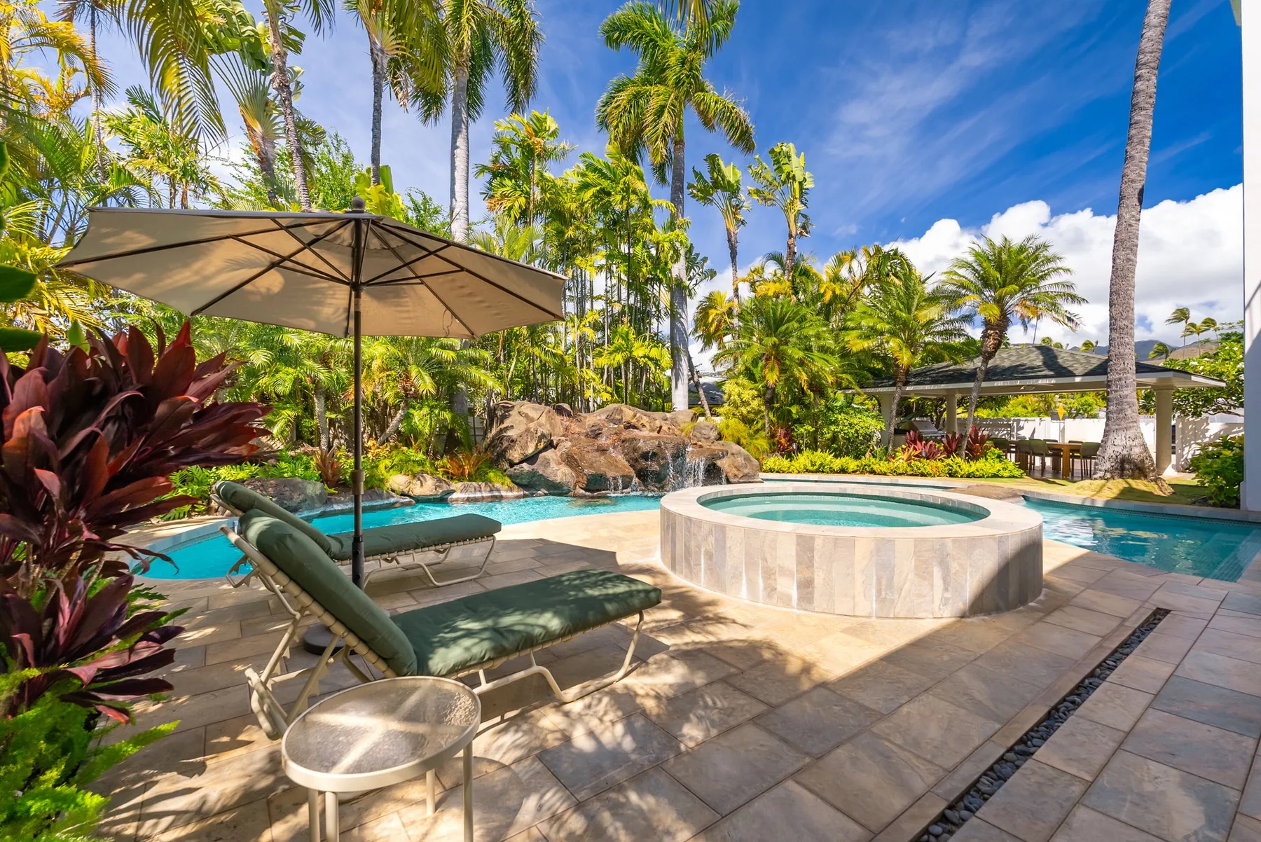 Una piscina exterior y un spa redondo están rodeados de palmeras y asientos de patio.
