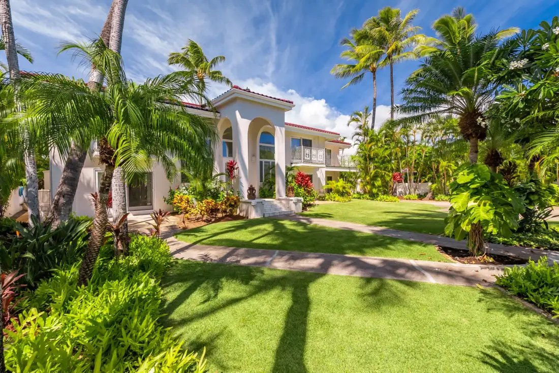 Un jardín ajardinado rodea un edificio blanco bajo altas palmeras.