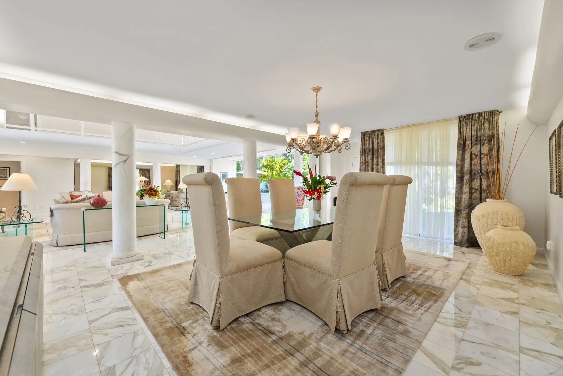 Comedor con asientos tapizados alrededor de una mesa de vidrio, junto a grandes ventanas con cortinas.