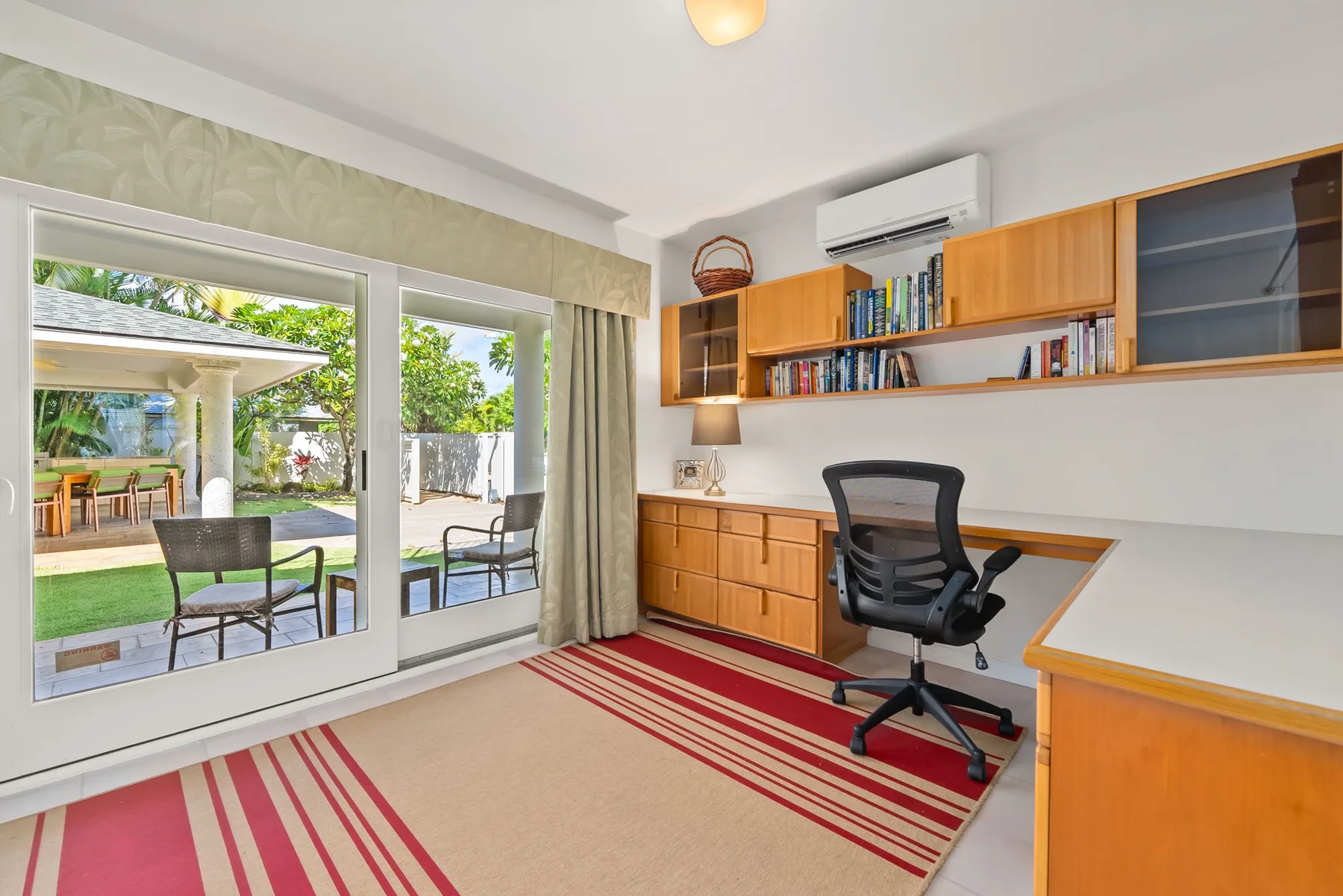 Un despacho en casa con escritorio y silla junto a grandes ventanas con vistas a un jardín.