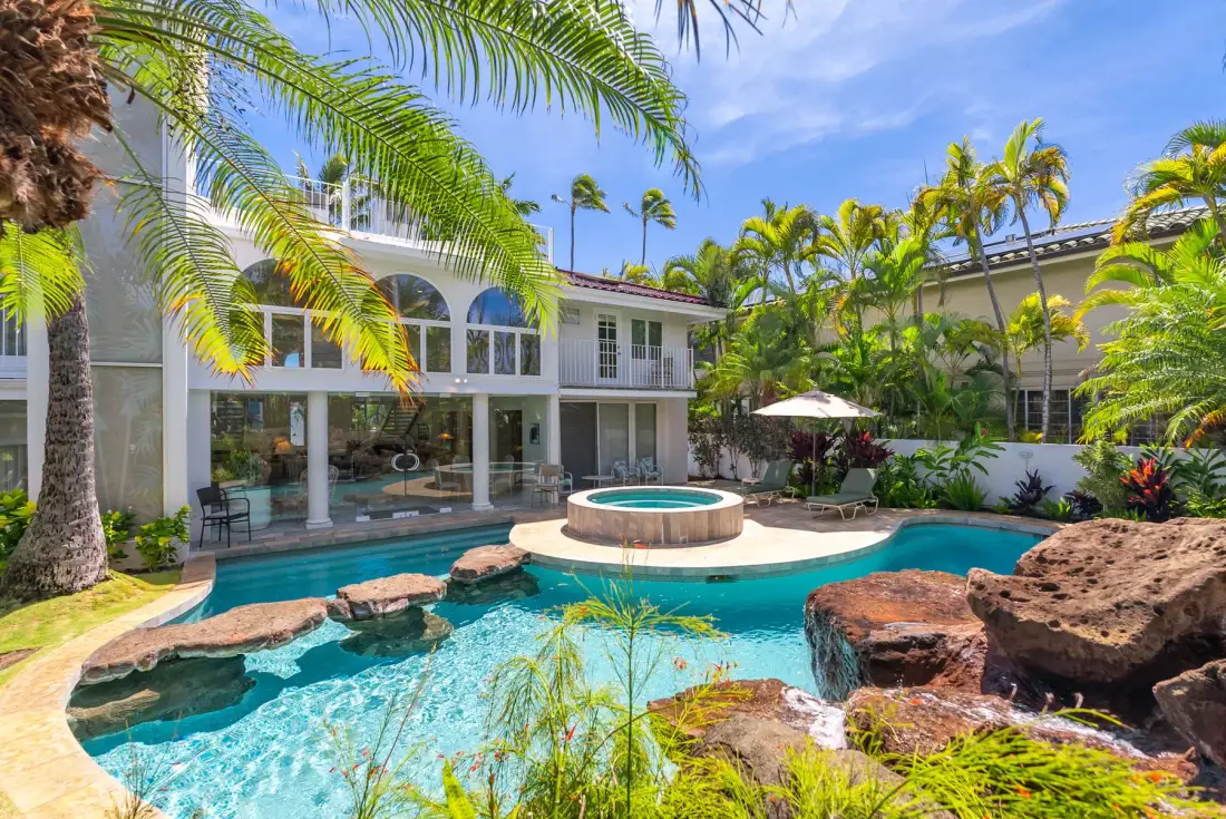 Una piscina en un patio tropical junto a un edificio blanco y vegetación frondosa.