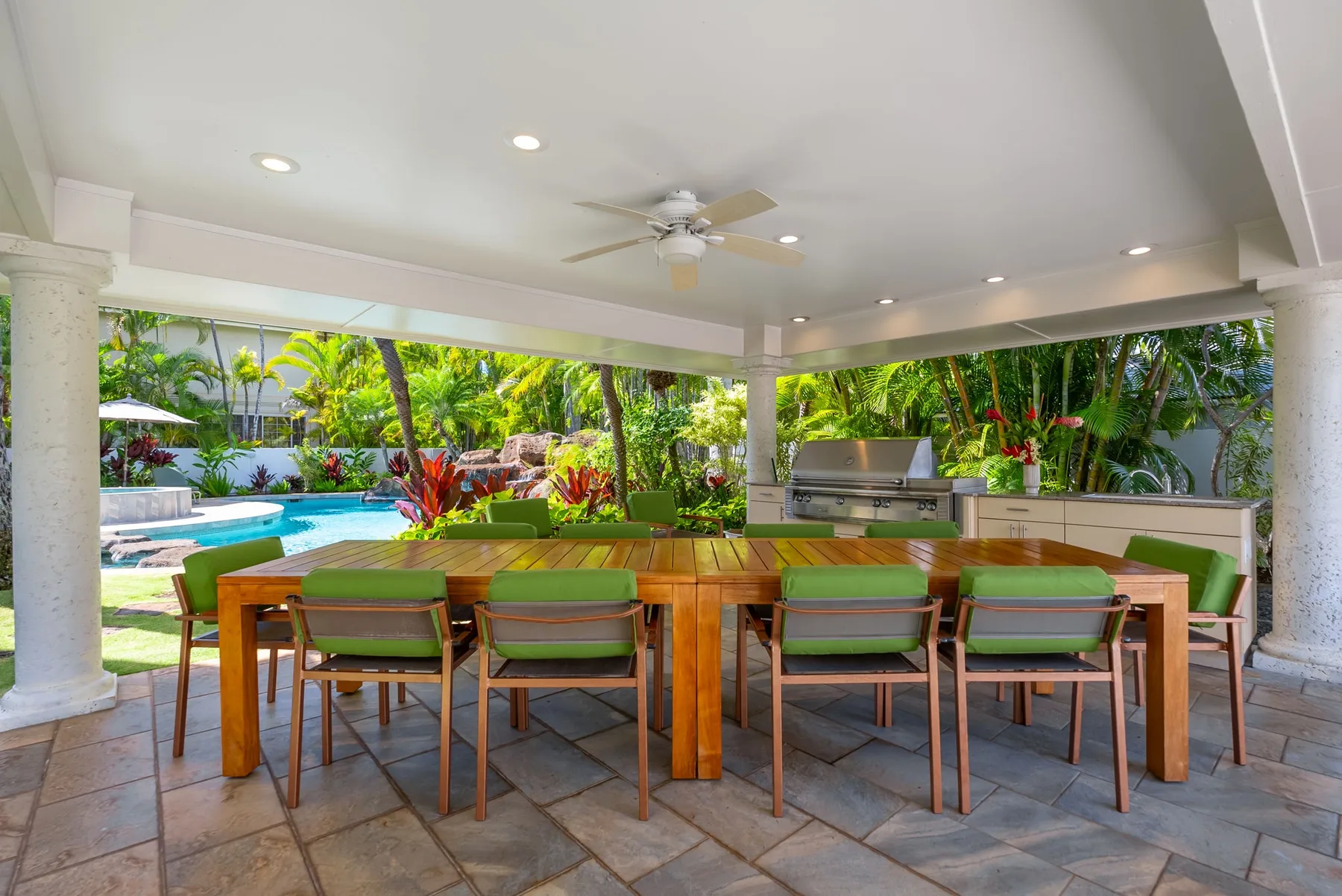 Un comedor exterior cubierto da a una piscina y un jardín tropical.