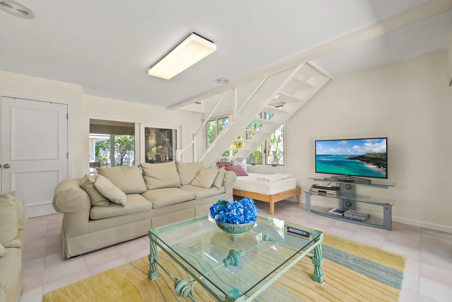 Una sala de estar luminosa con asientos, una mesa de centro de vidrio y un televisor.