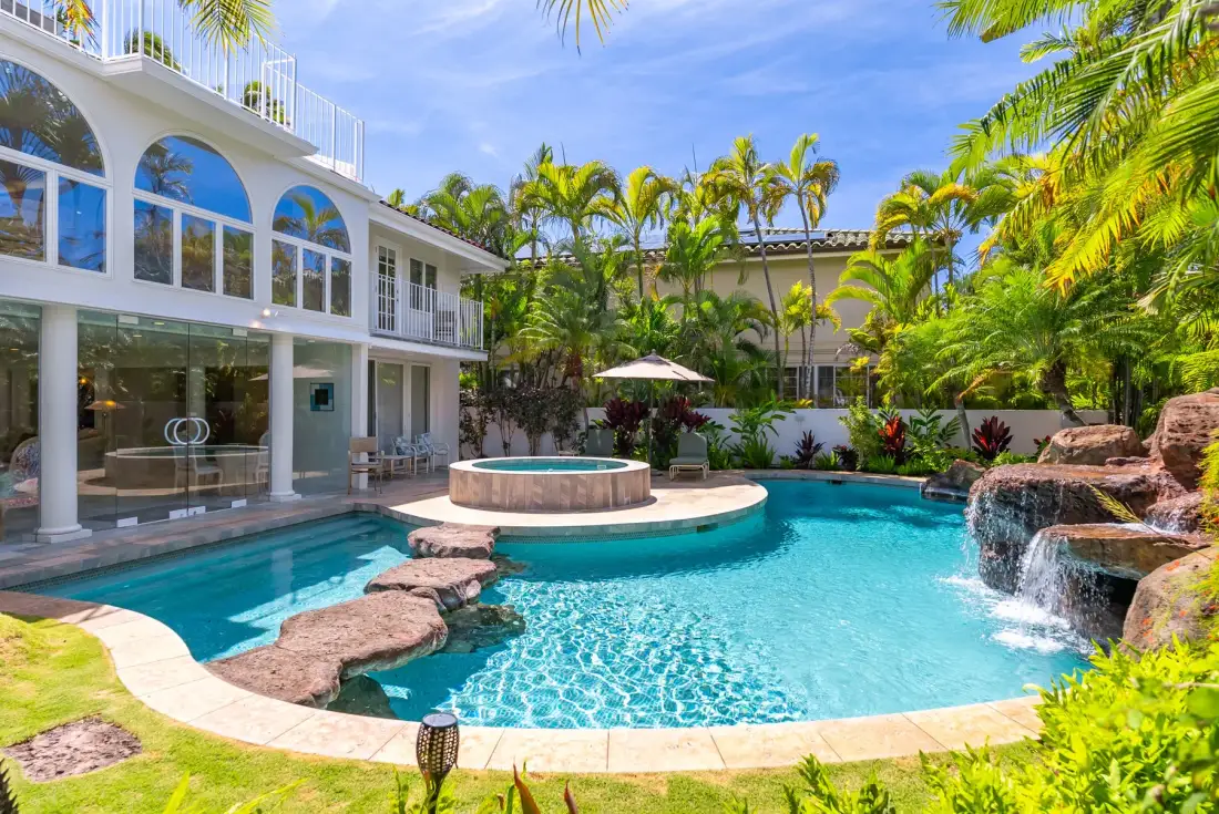 Una piscina en un patio tropical está junto a un edificio acristalado y jardines.