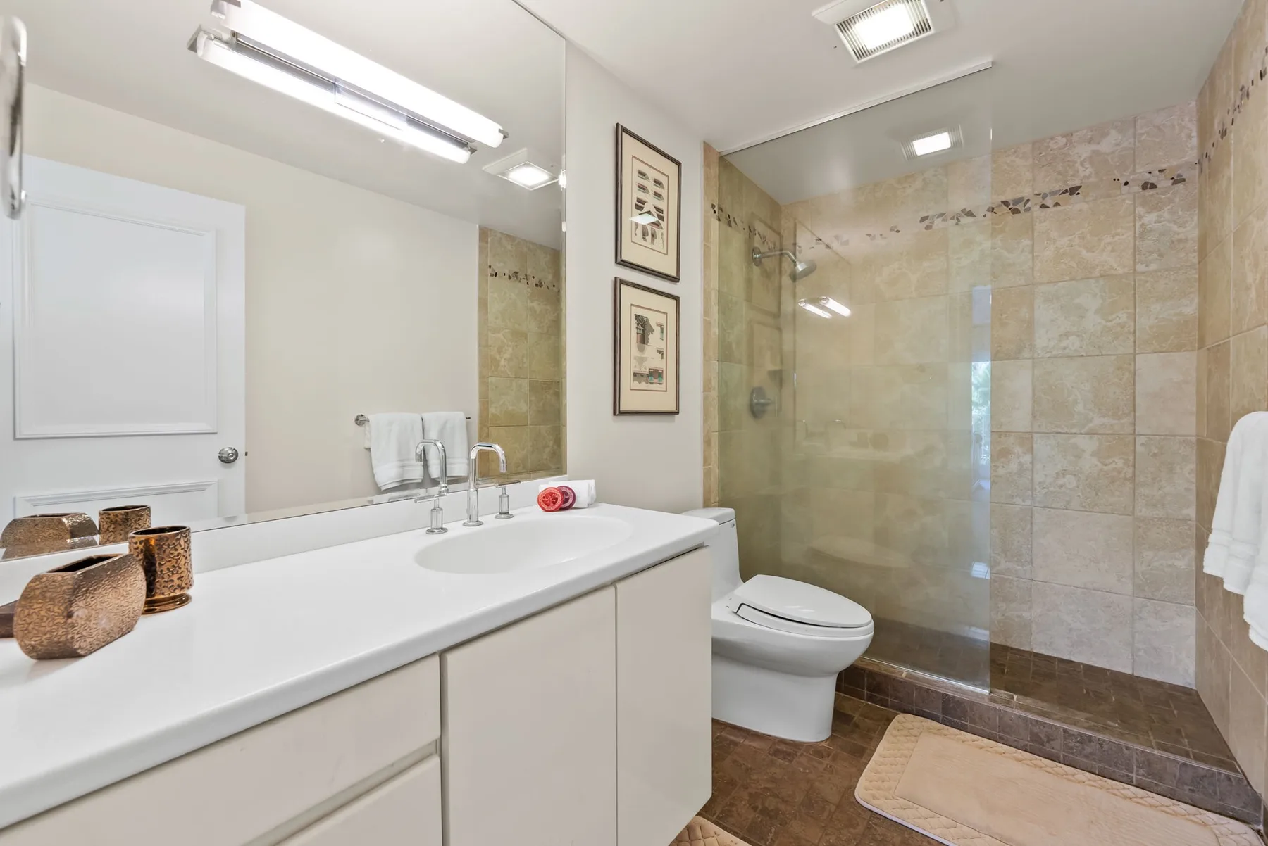 Un baño luminoso con un tocador largo, un inodoro y una ducha con mampara de vidrio.