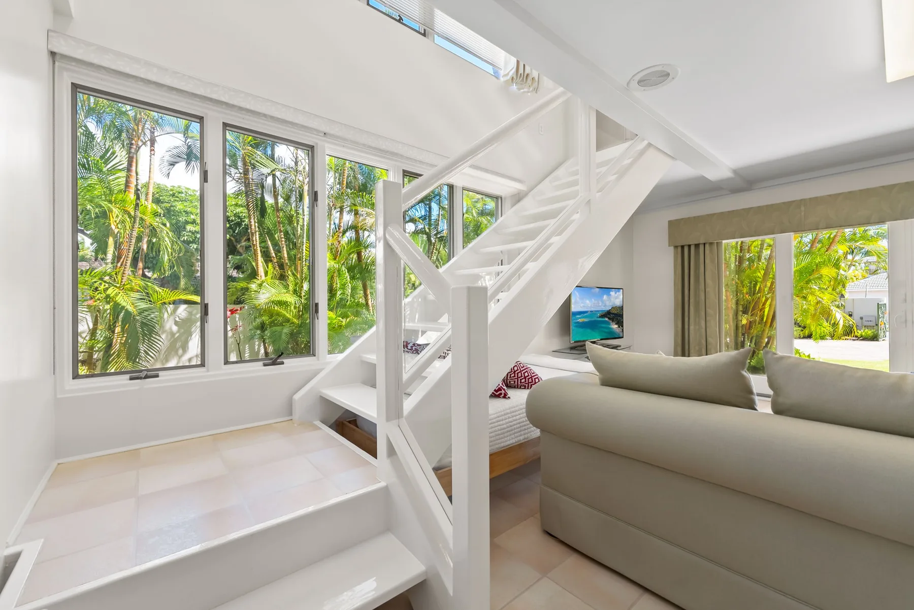 Una sala luminosa con una escalera blanca y grandes ventanas con vistas a la vegetación.