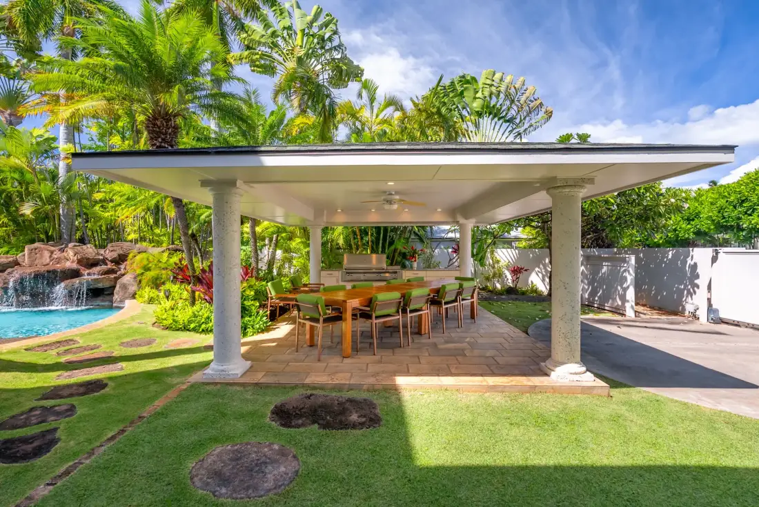 Una zona de comedor al aire libre está bajo un patio cubierto junto a una piscina.