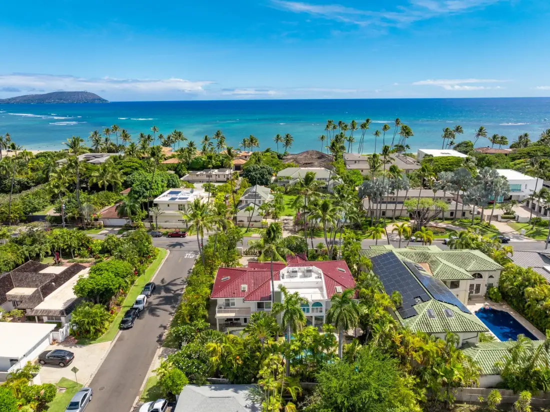 Vista aérea de un vecindario costero tropical con casas, palmeras y el océano.