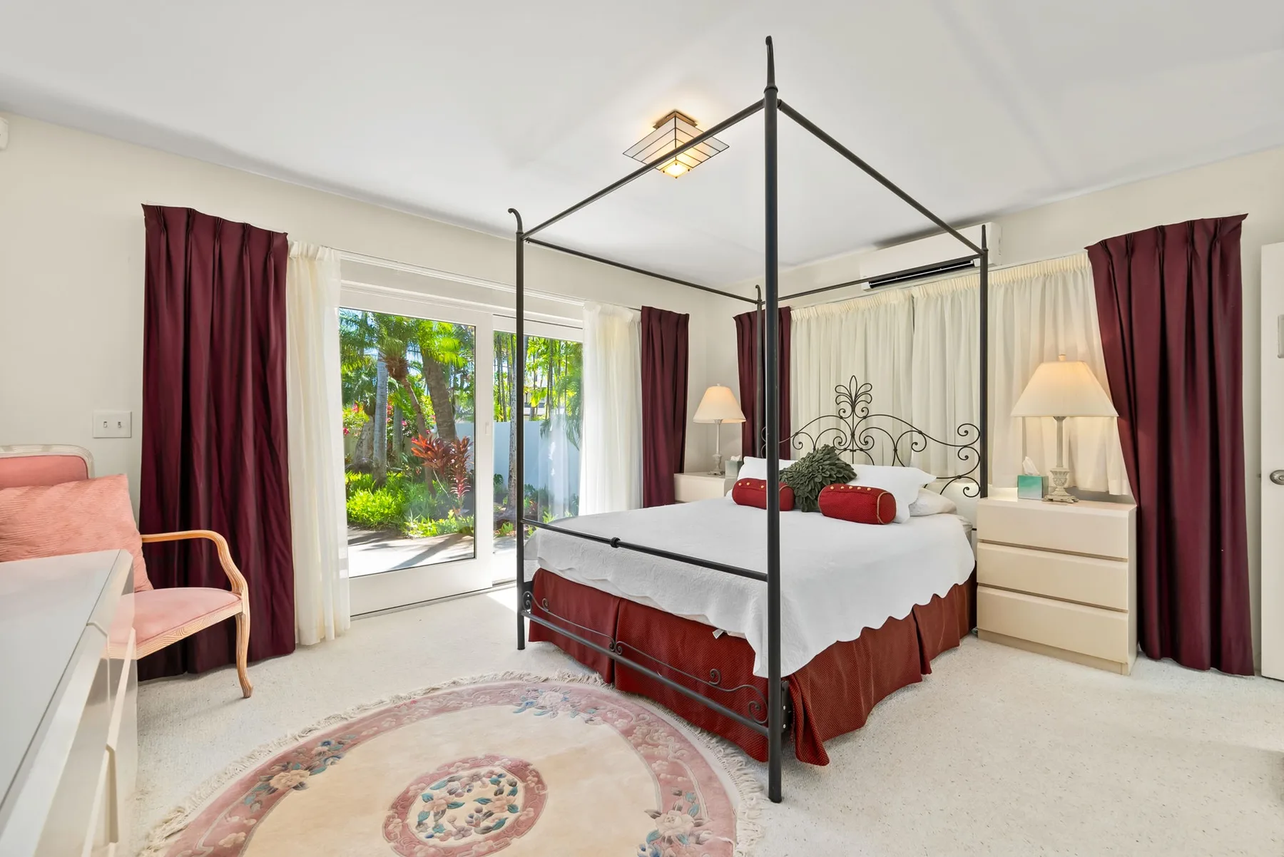 Un dormitorio luminoso con una cama con dosel negra y puertas de vidrio que dan al jardín.