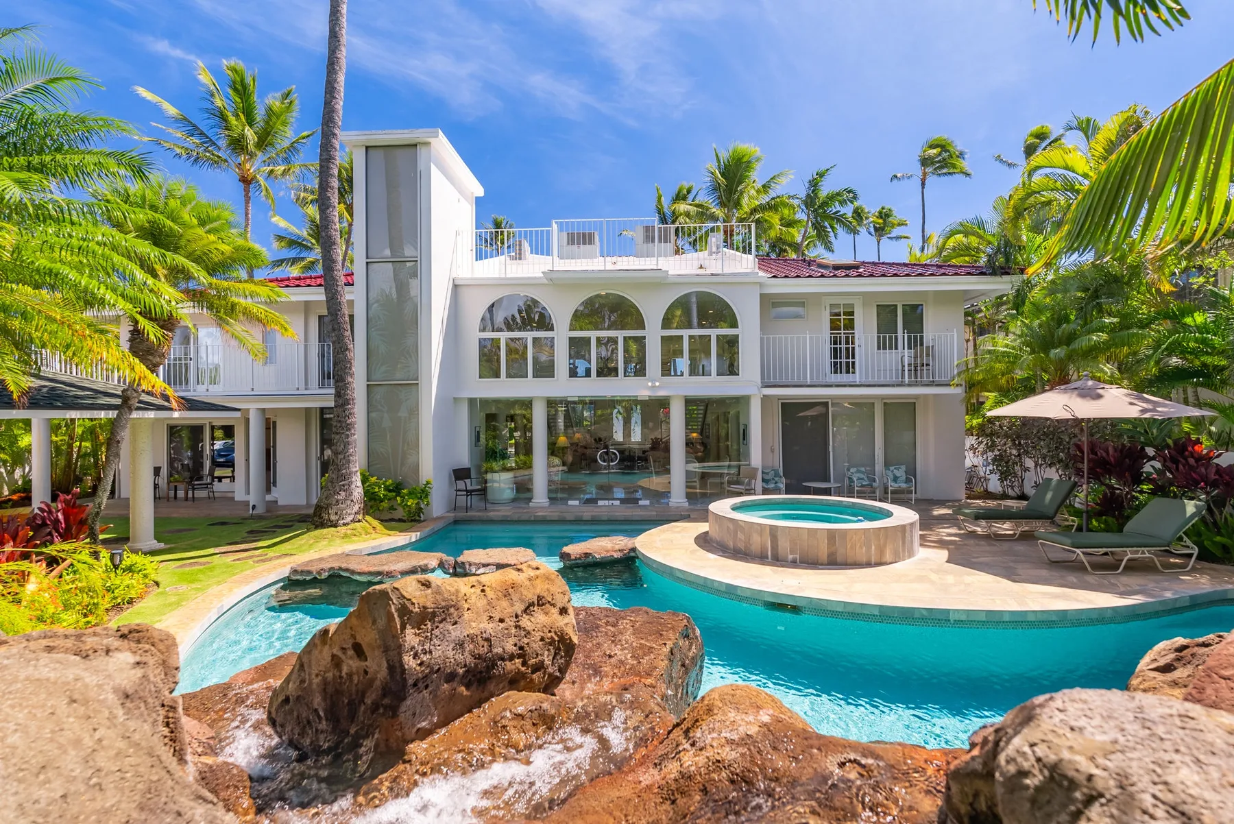 Una casa blanca de estilo tropical está junto a una piscina curva y un elemento acuático rocoso.