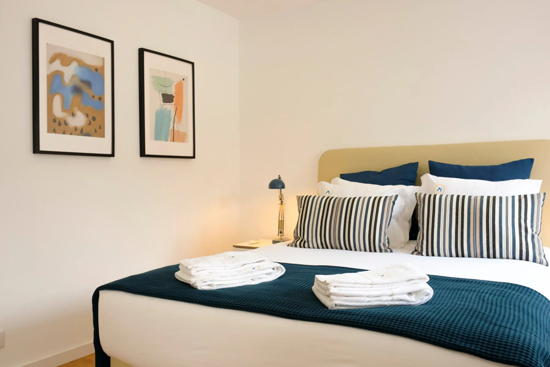 Un dormitorio con una cama bien arreglada y cuadros enmarcados en la pared.