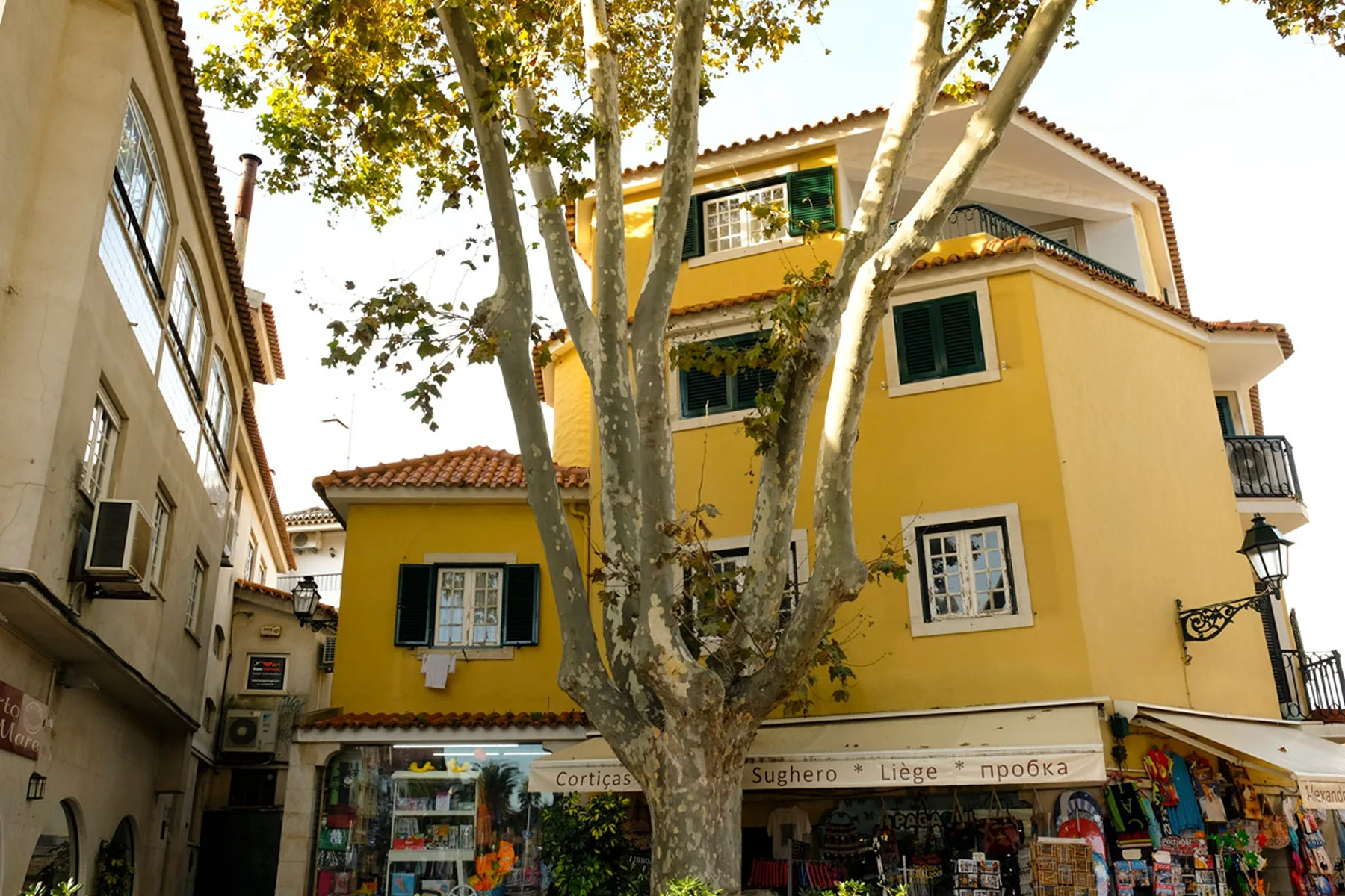 Un edificio amarillo con contraventanas verdes y tiendas a pie de calle.