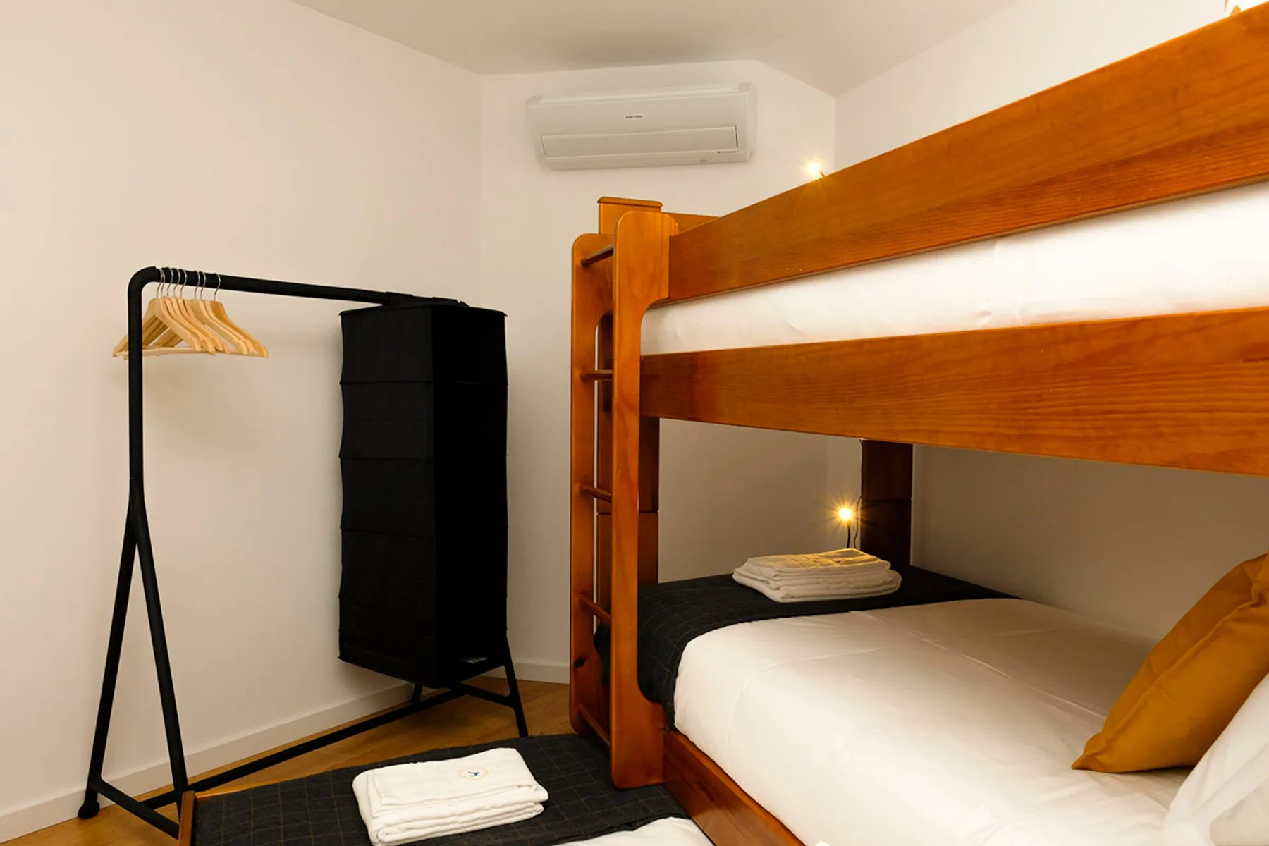 Un dormitorio con una litera de madera, un perchero y toallas dobladas.
