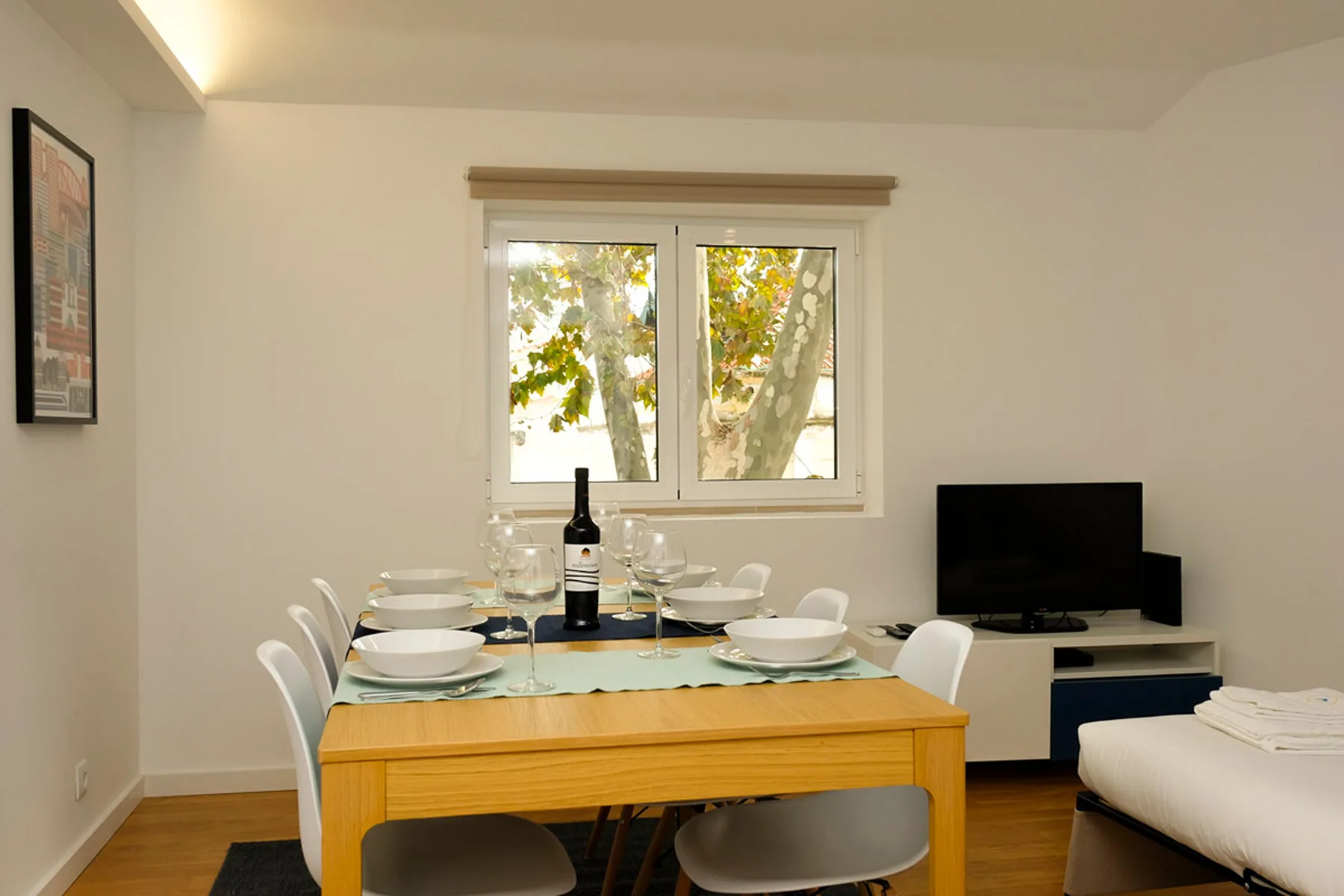 Comedor con la mesa puesta junto a una ventana y un televisor.