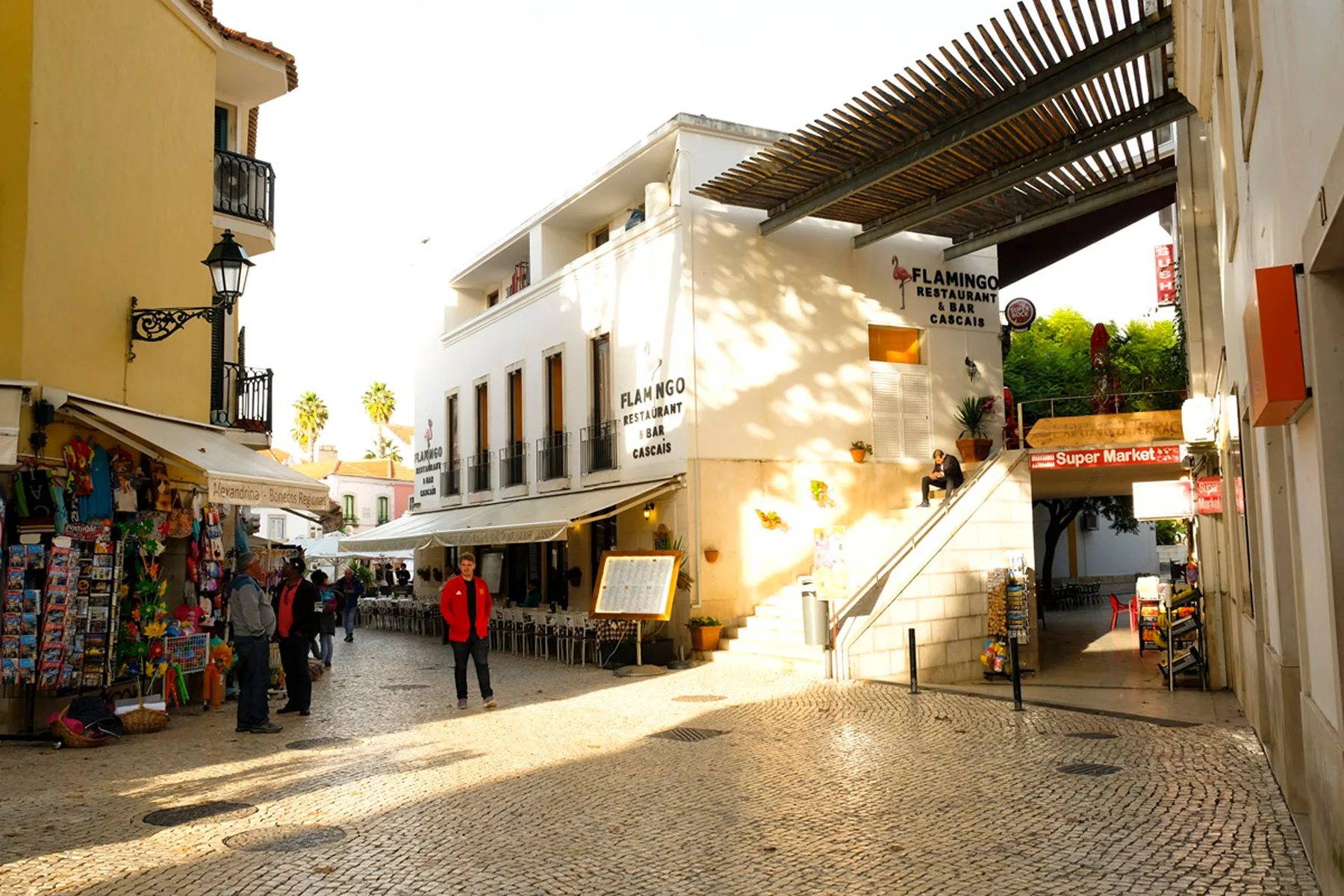 Una calle peatonal soleada con tiendas, cafés y pavimento de adoquines.