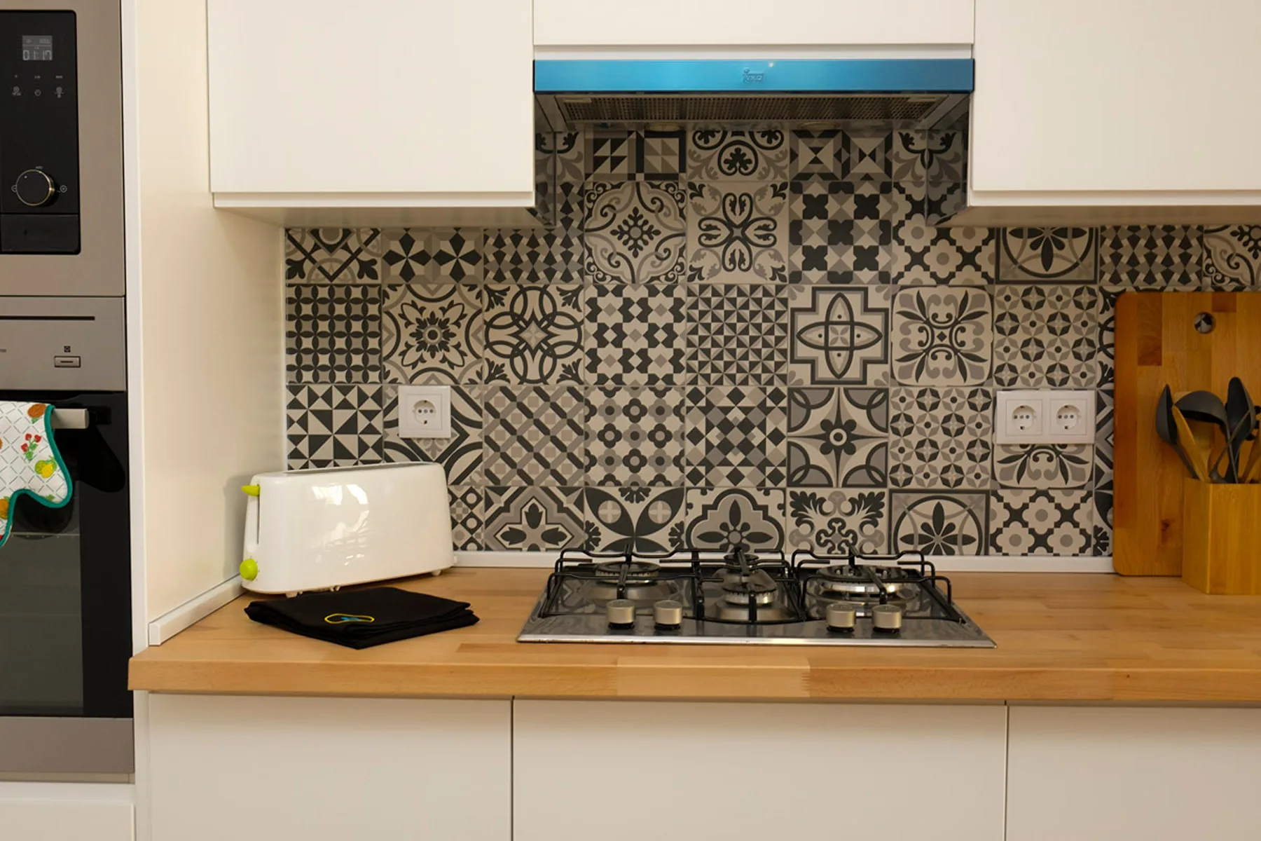 Una cocina con una placa de gas bajo un salpicadero de azulejos estampados.