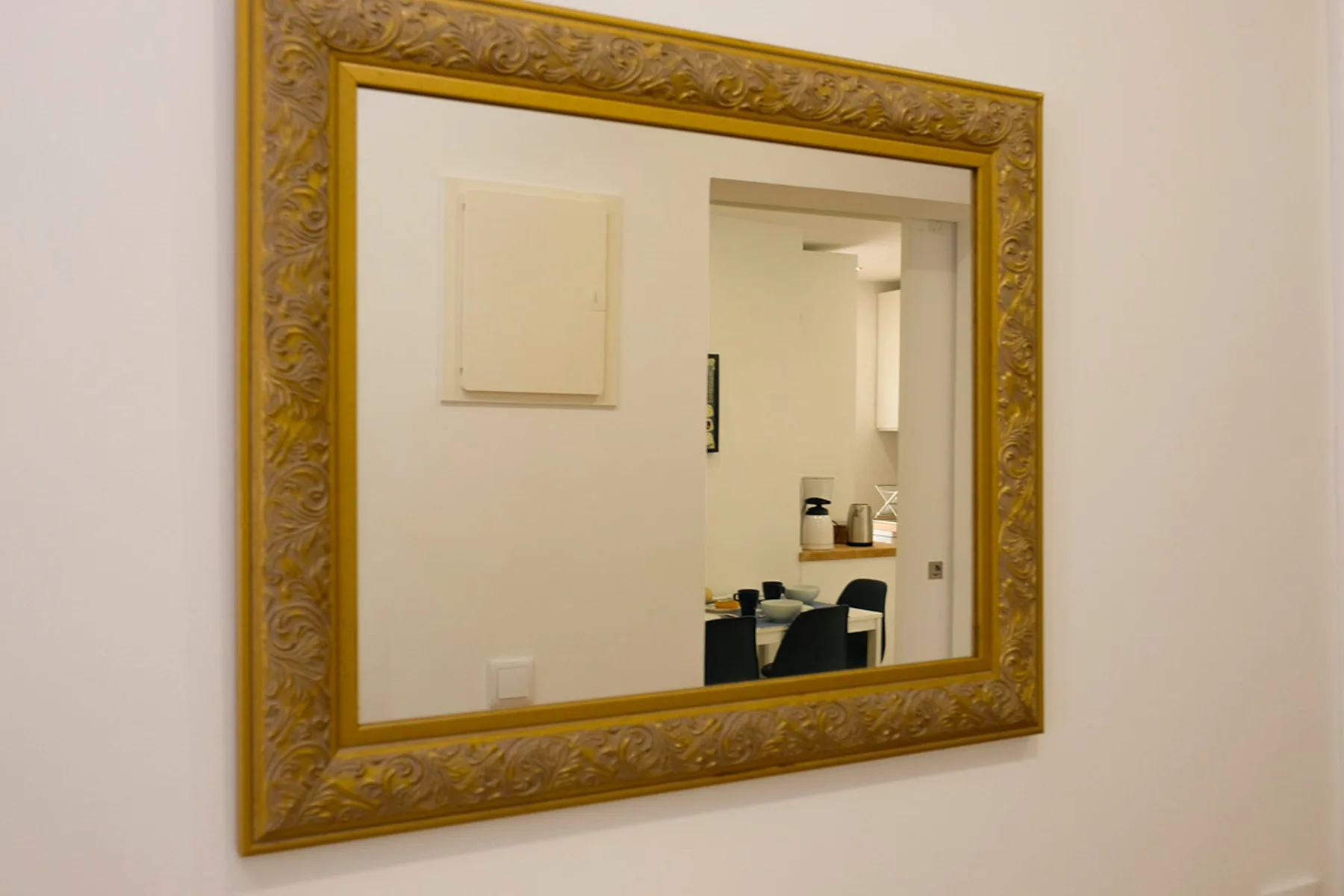 Un espejo grande y ornamentado cuelga de una pared clara y refleja un comedor.